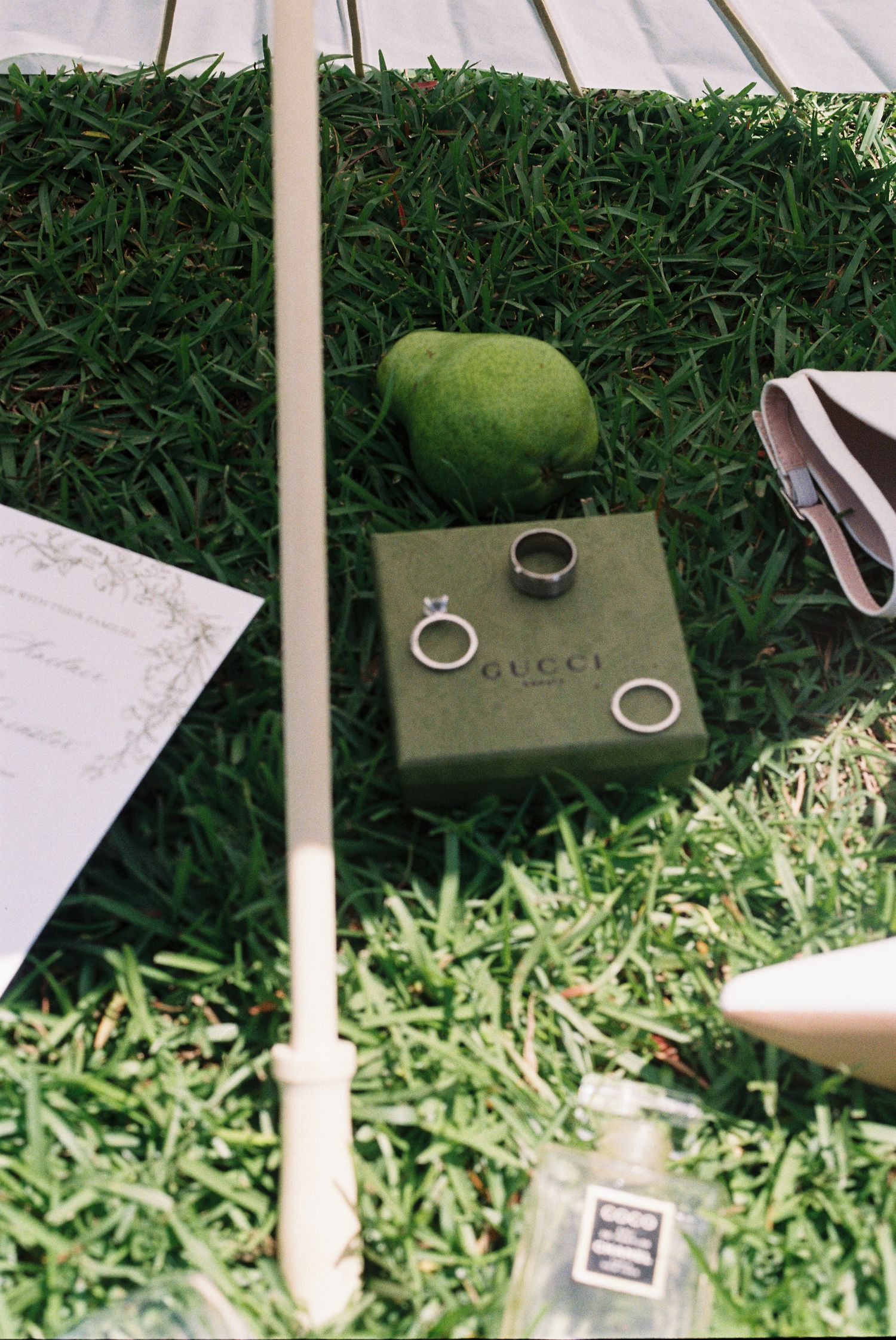 Wedding rings and decorative elements arranged on grass with a white parasol.