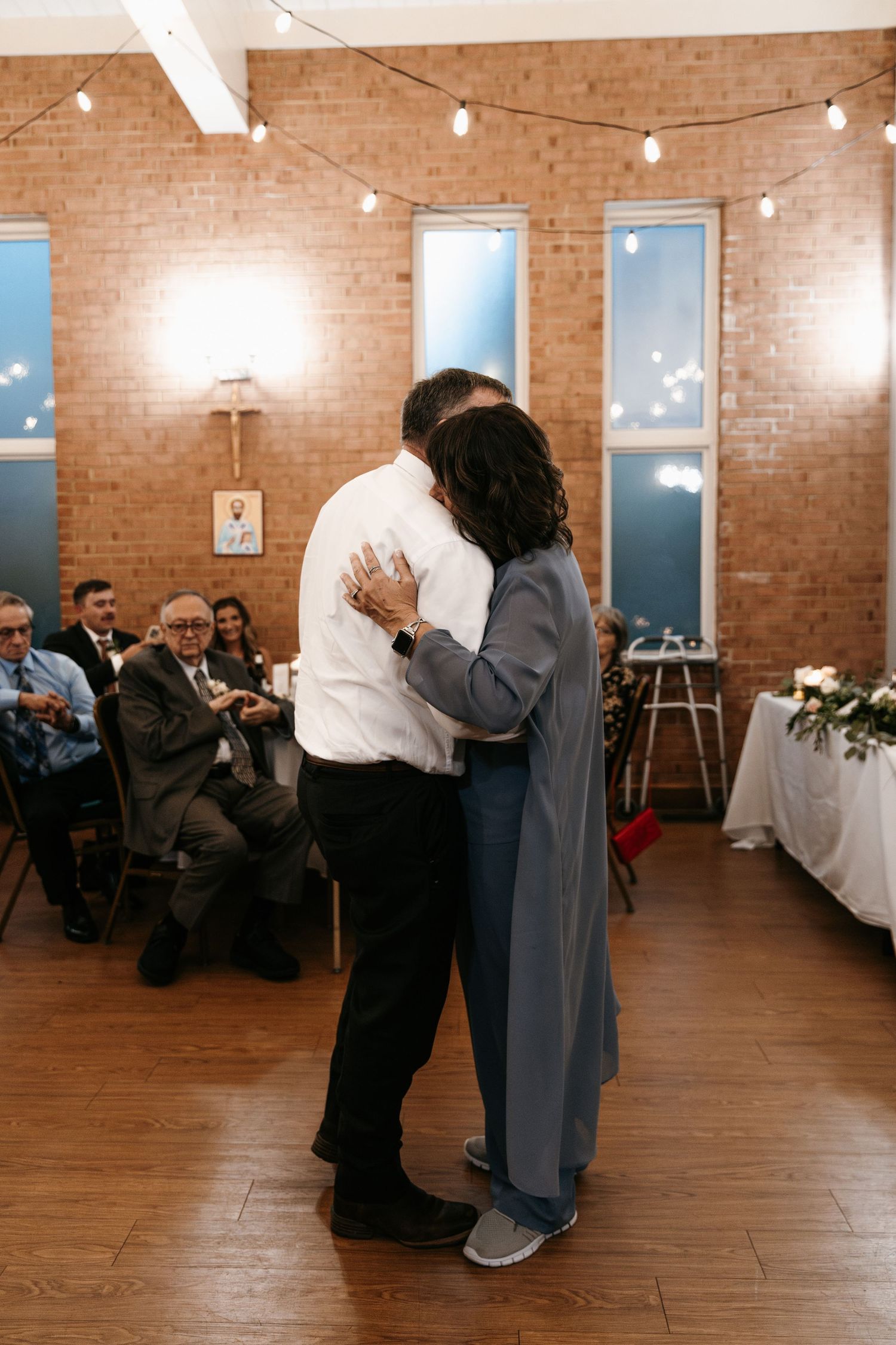 Couples dancing together in an elegant brick-walled reception space with overhead string lighting.