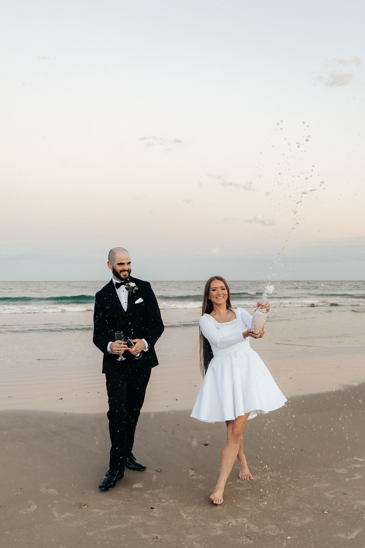 A couple celebrating with champagne on the beach at sunset.
