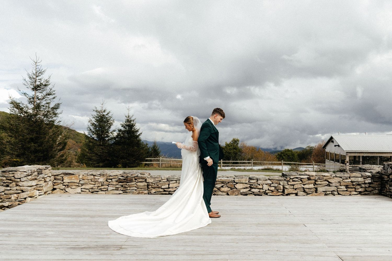 Bride and groom share a romantic first look on a stone patio with mountain views and cloudy skies.