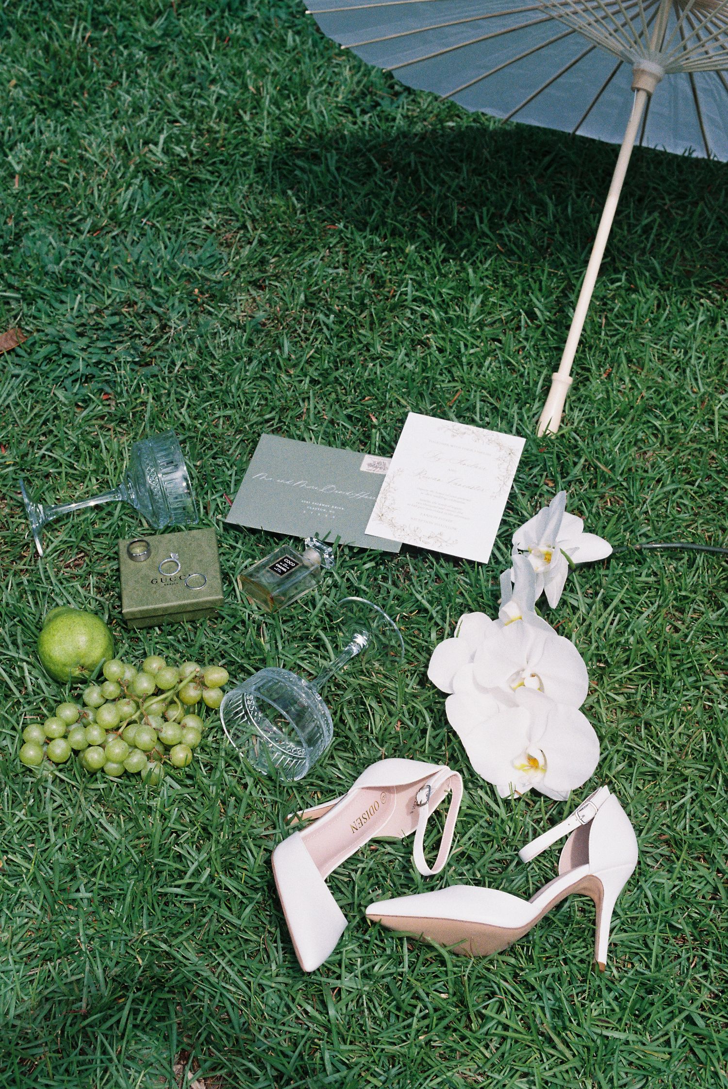 Wedding details including parasol, shoes, and grapes artfully arranged on grass.