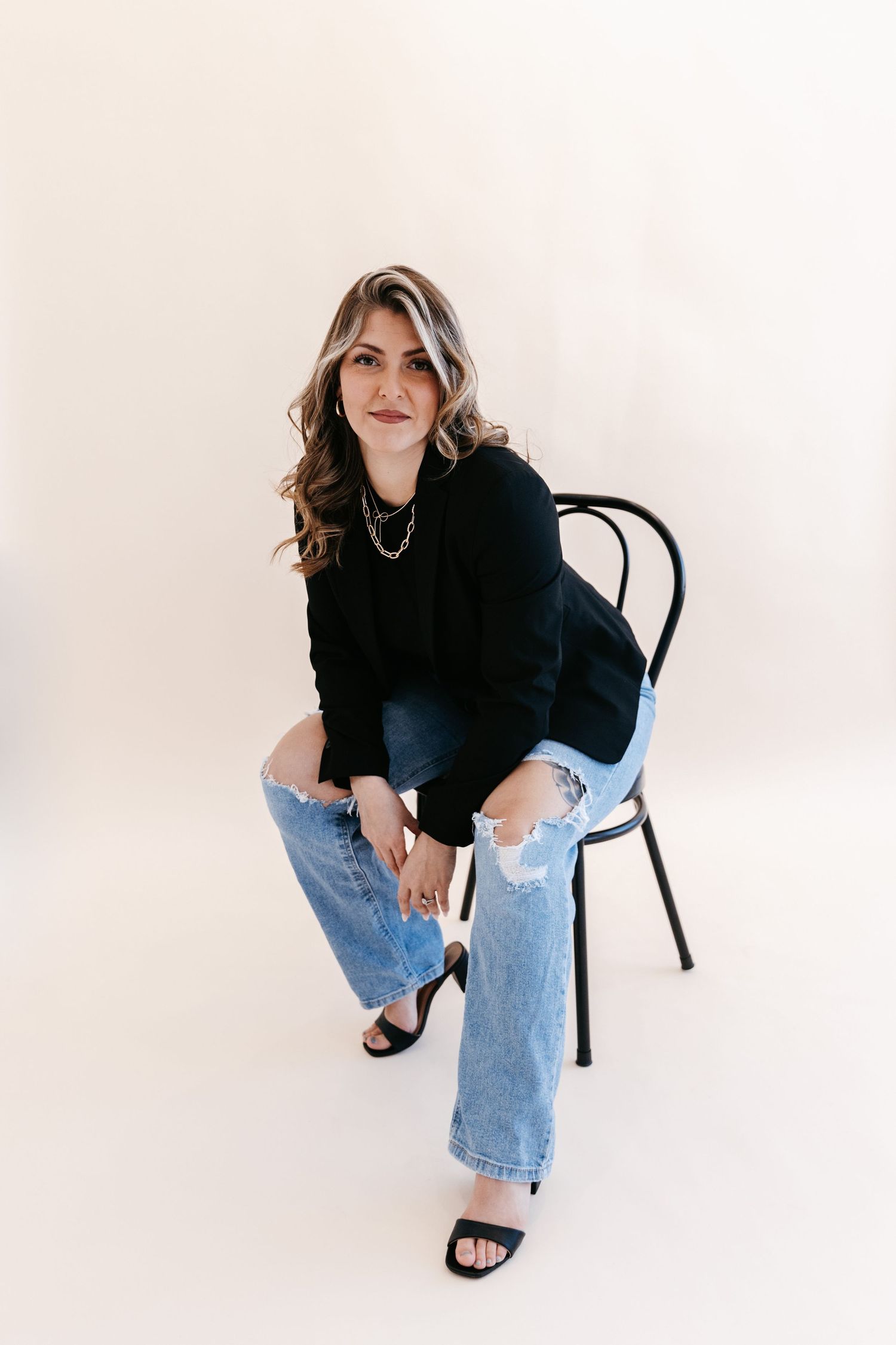 Studio portrait of a woman in casual denim and black top seated on chair against white background.