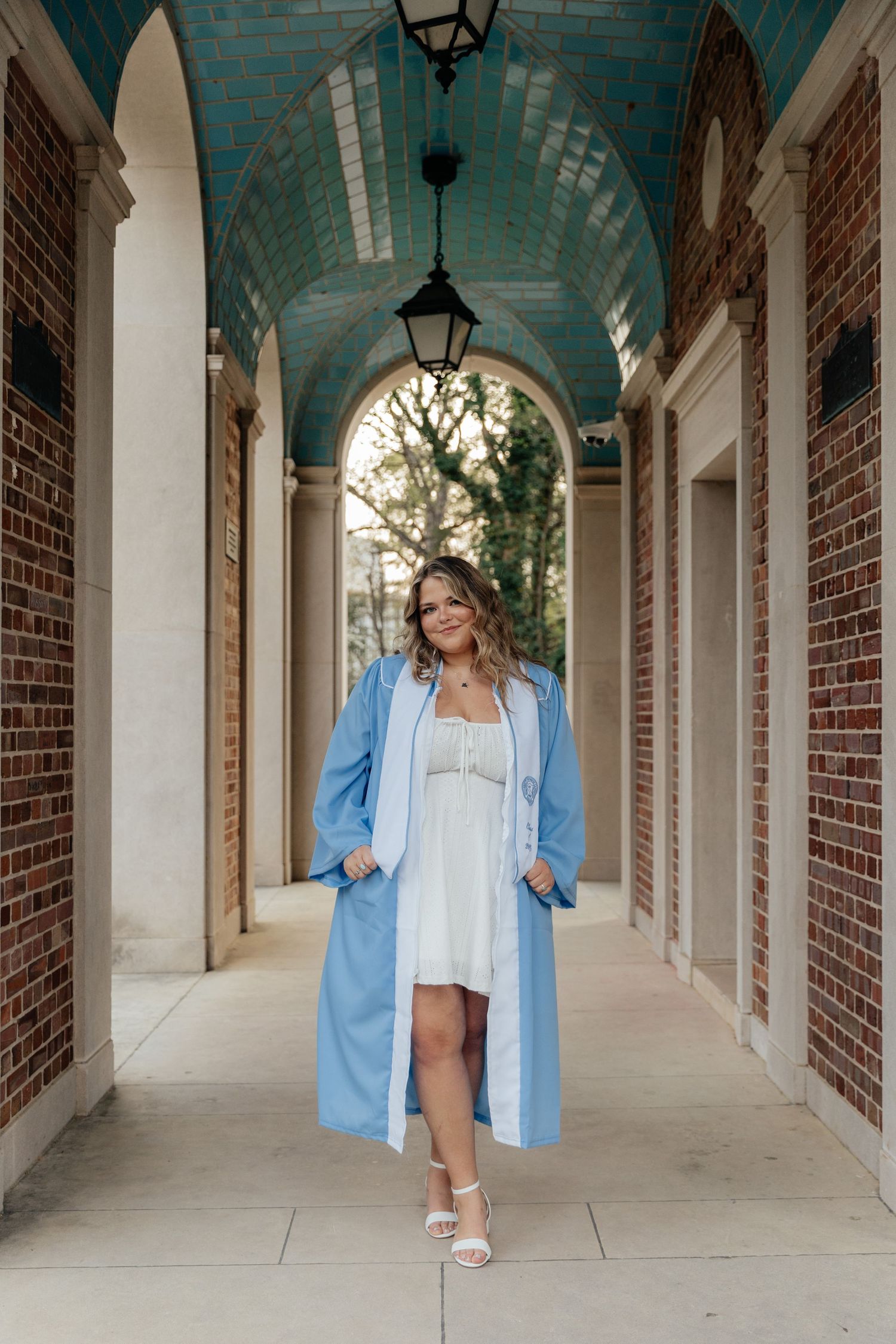 Graduate in light blue gown poses confidently in elegant brick and stone archway.