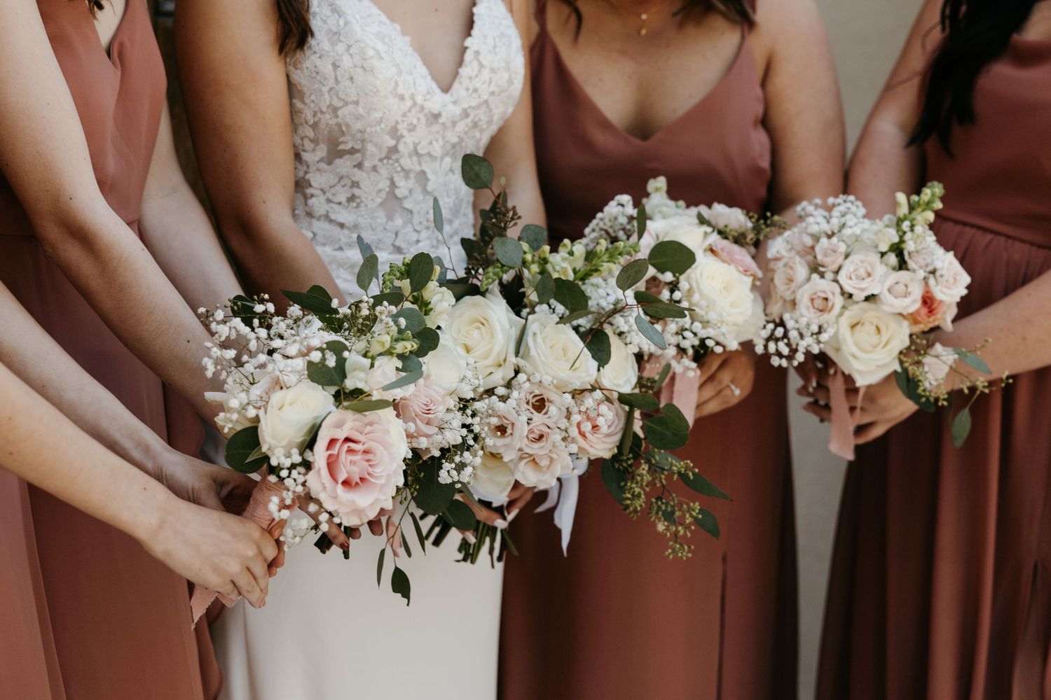 Close-up details of wedding bouquets with white and pink roses held by bridal party.