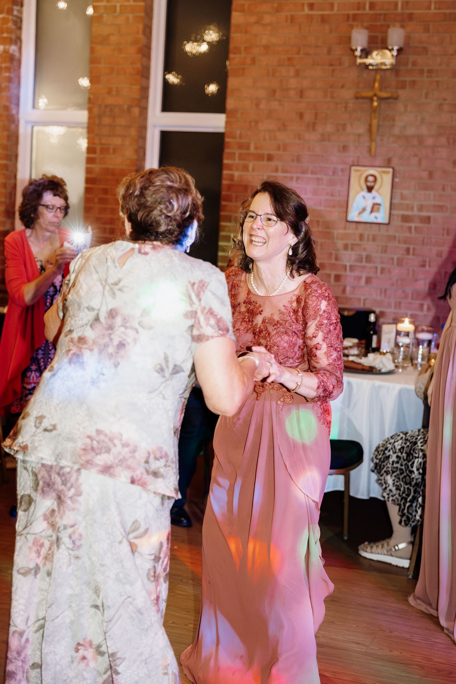 Wedding guests dancing and laughing together on the dance floor under warm lighting.