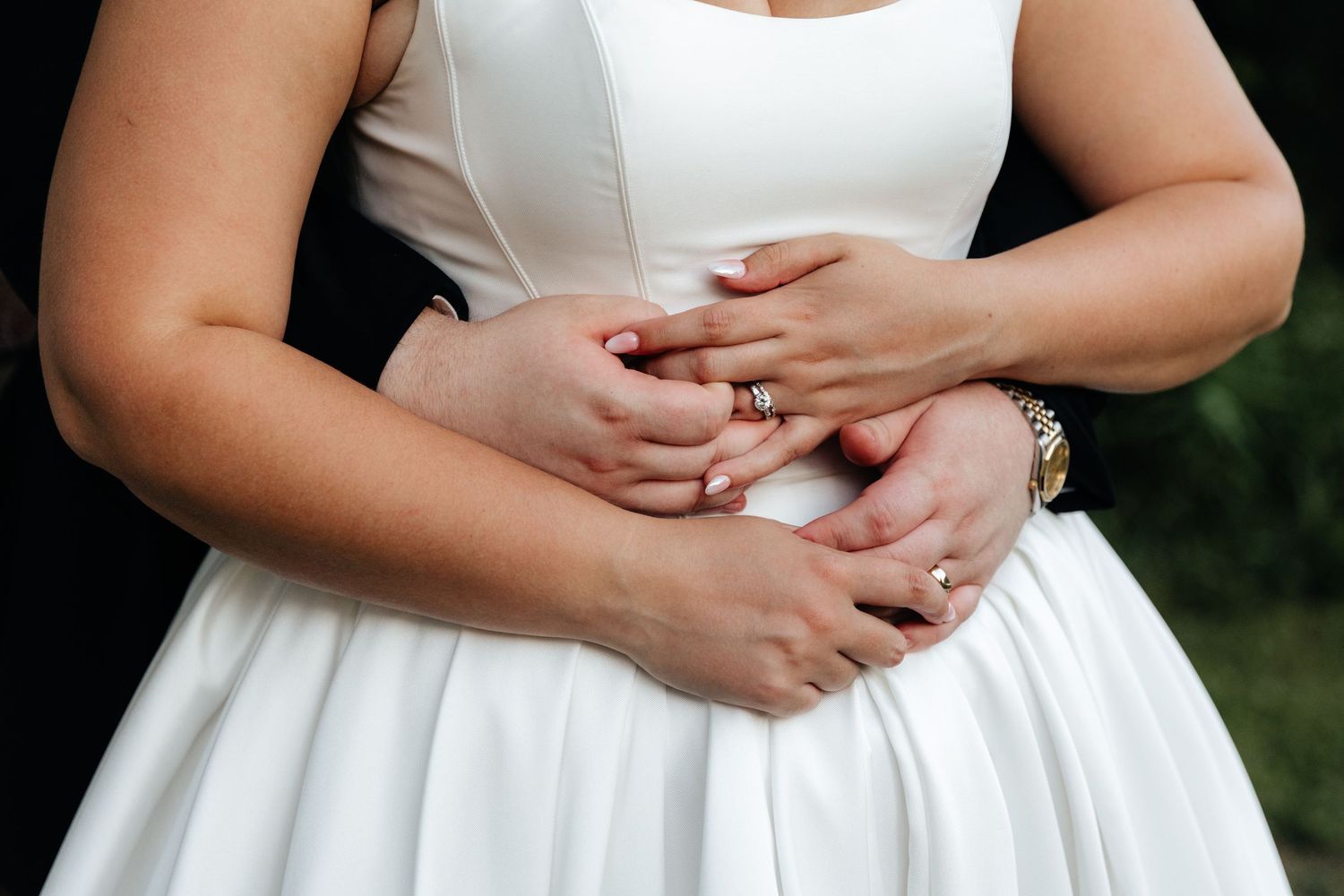 Close-up details of white wedding dress and hands.