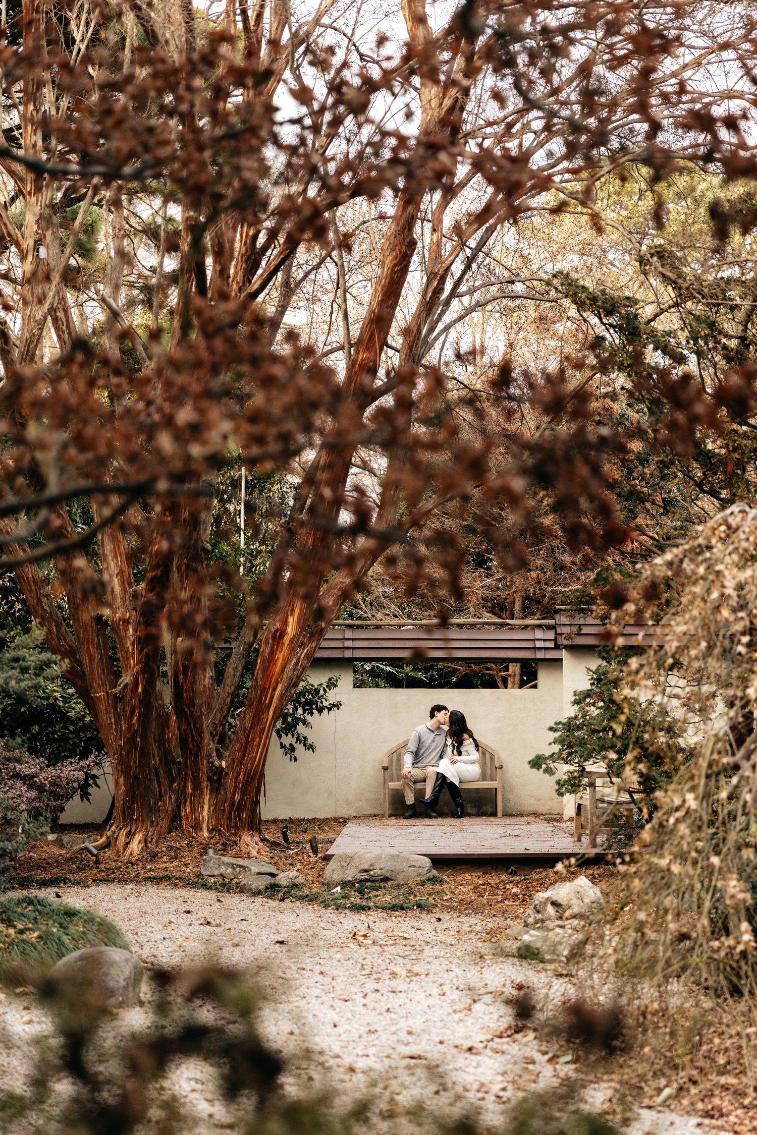 A romantic scene unfolds on a garden bench surrounded by autumn foliage.