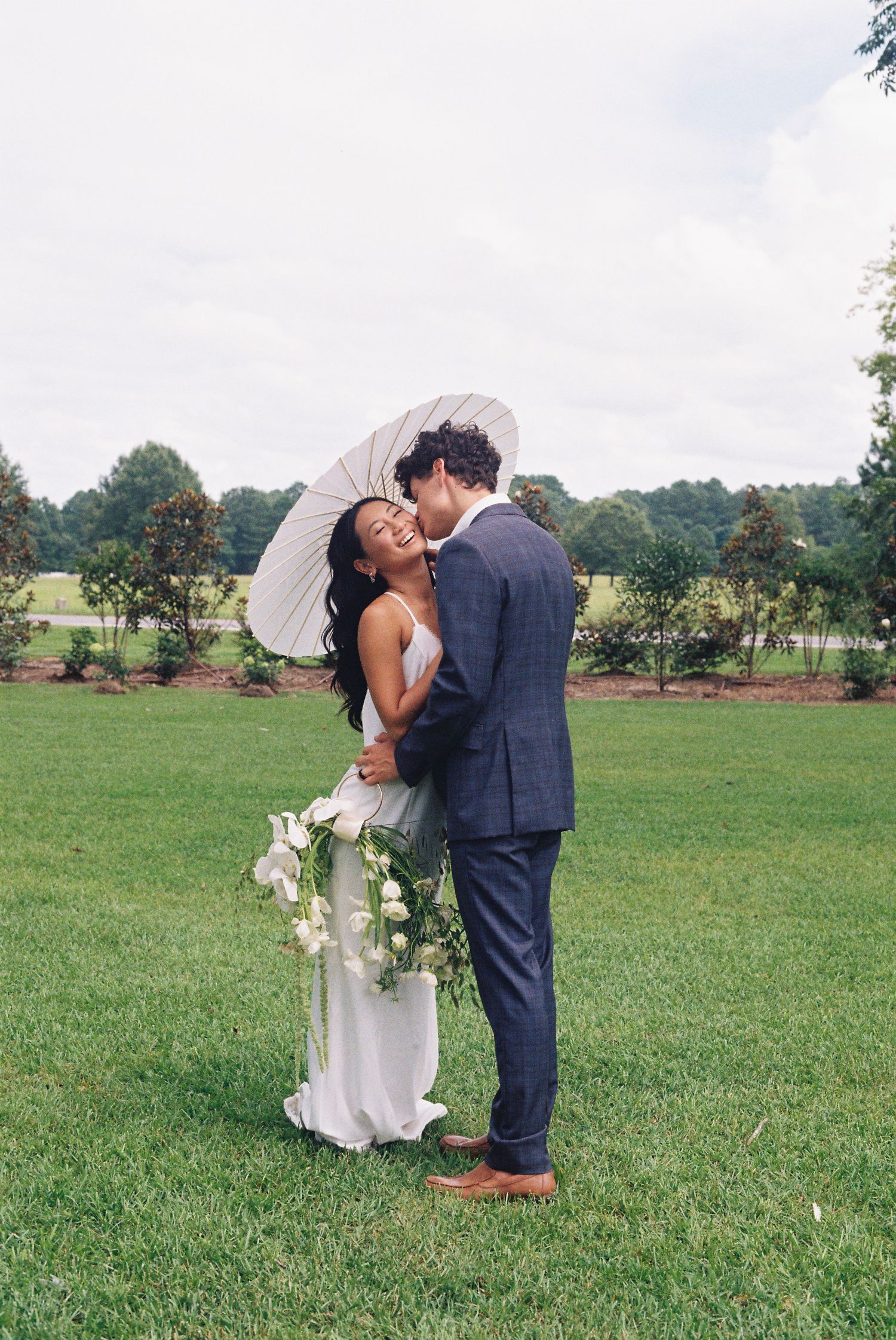 Couple shares intimate moments during outdoor wedding photoshoot on grassy field.