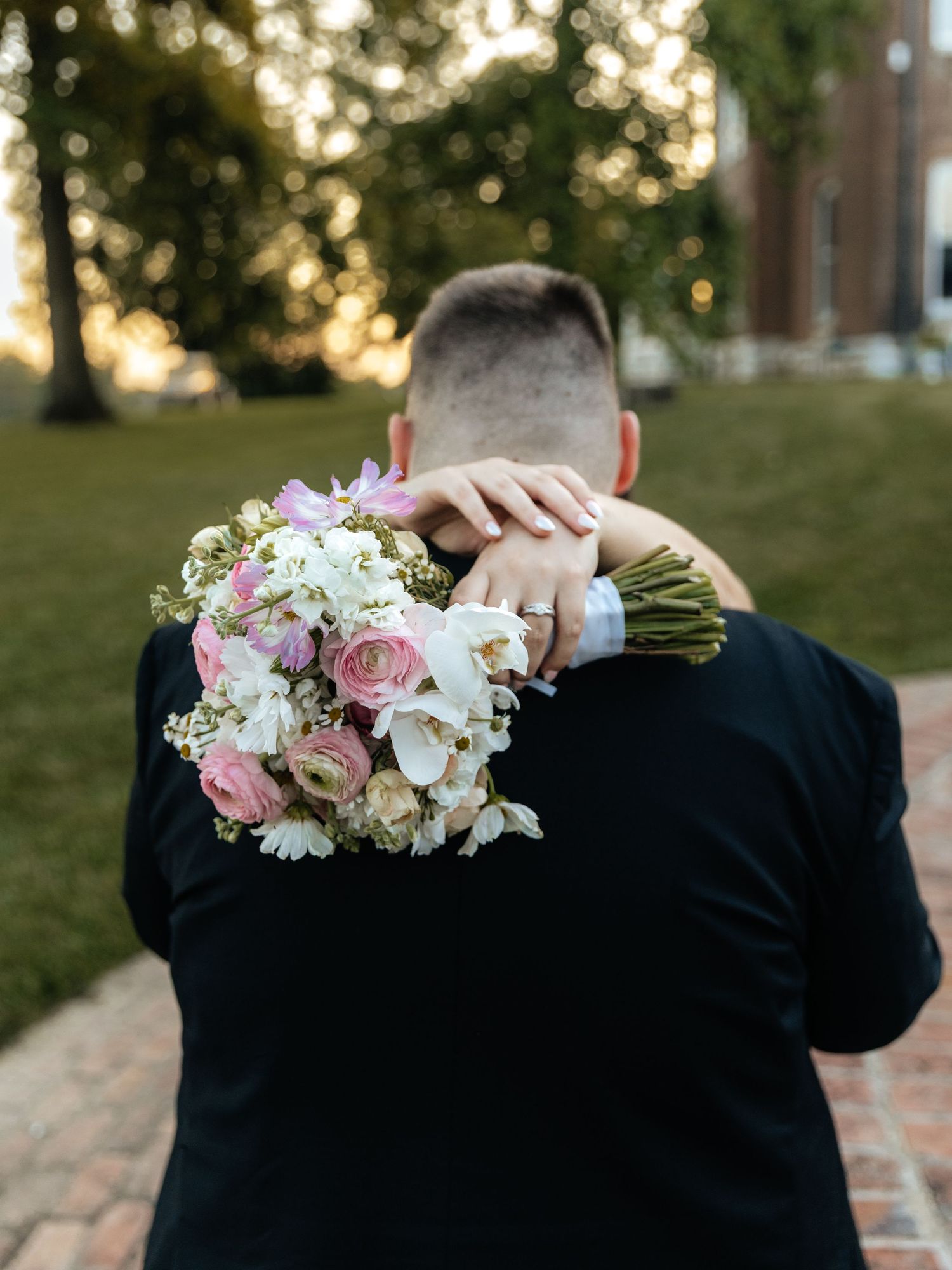 Close-up of pink and white wedding bouquet being held against a dark suit.