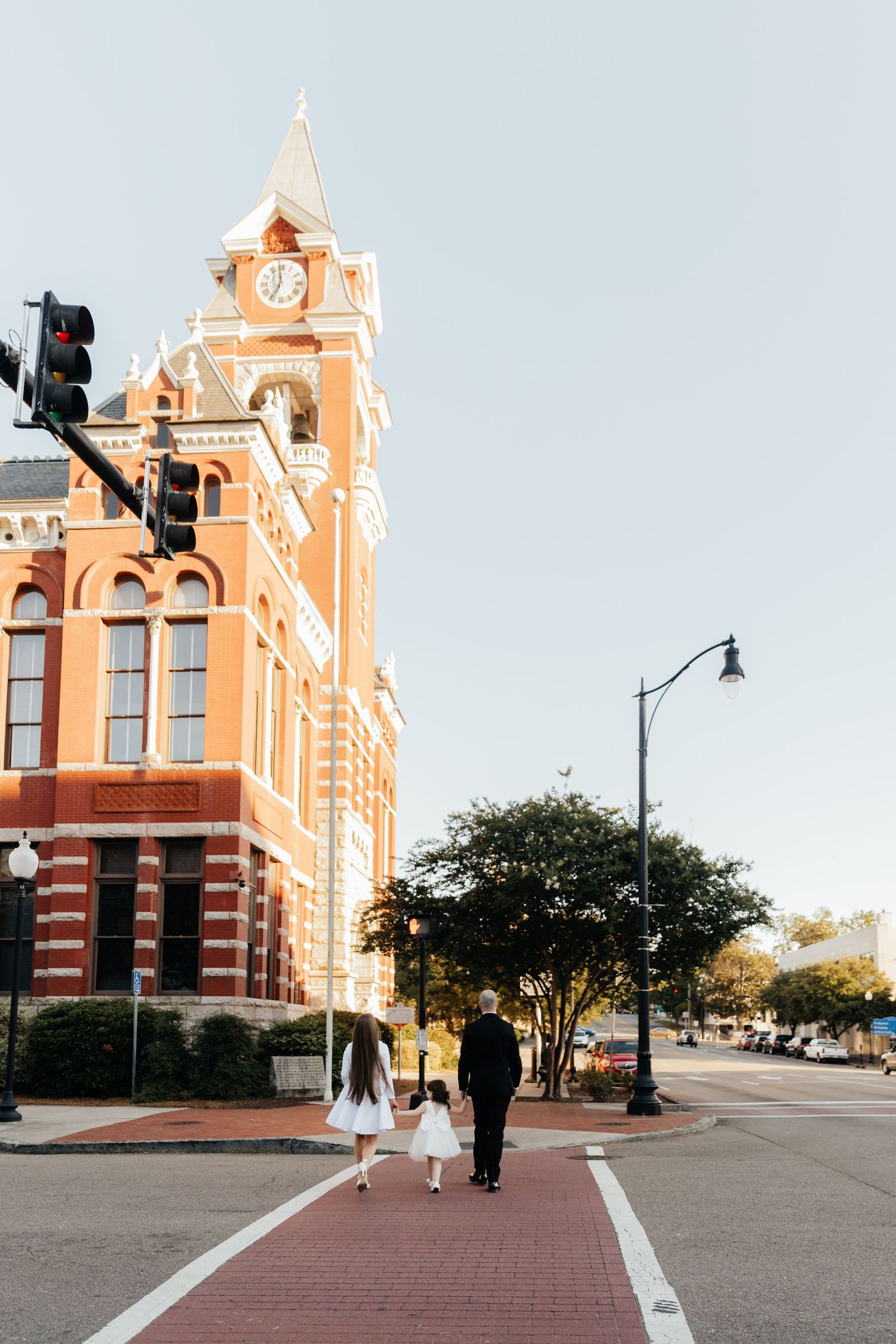 Family walking in front of historic brick building with clock tower photographed from street level on a clear day.