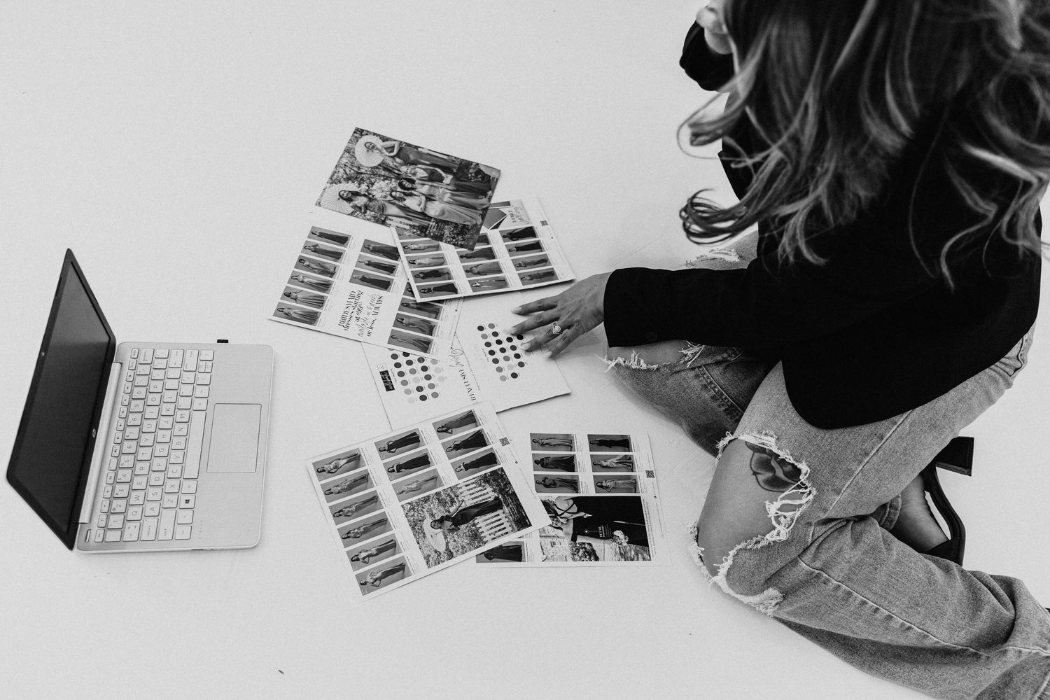 Black and white overhead shot of someone organizing magazine pages near laptop.