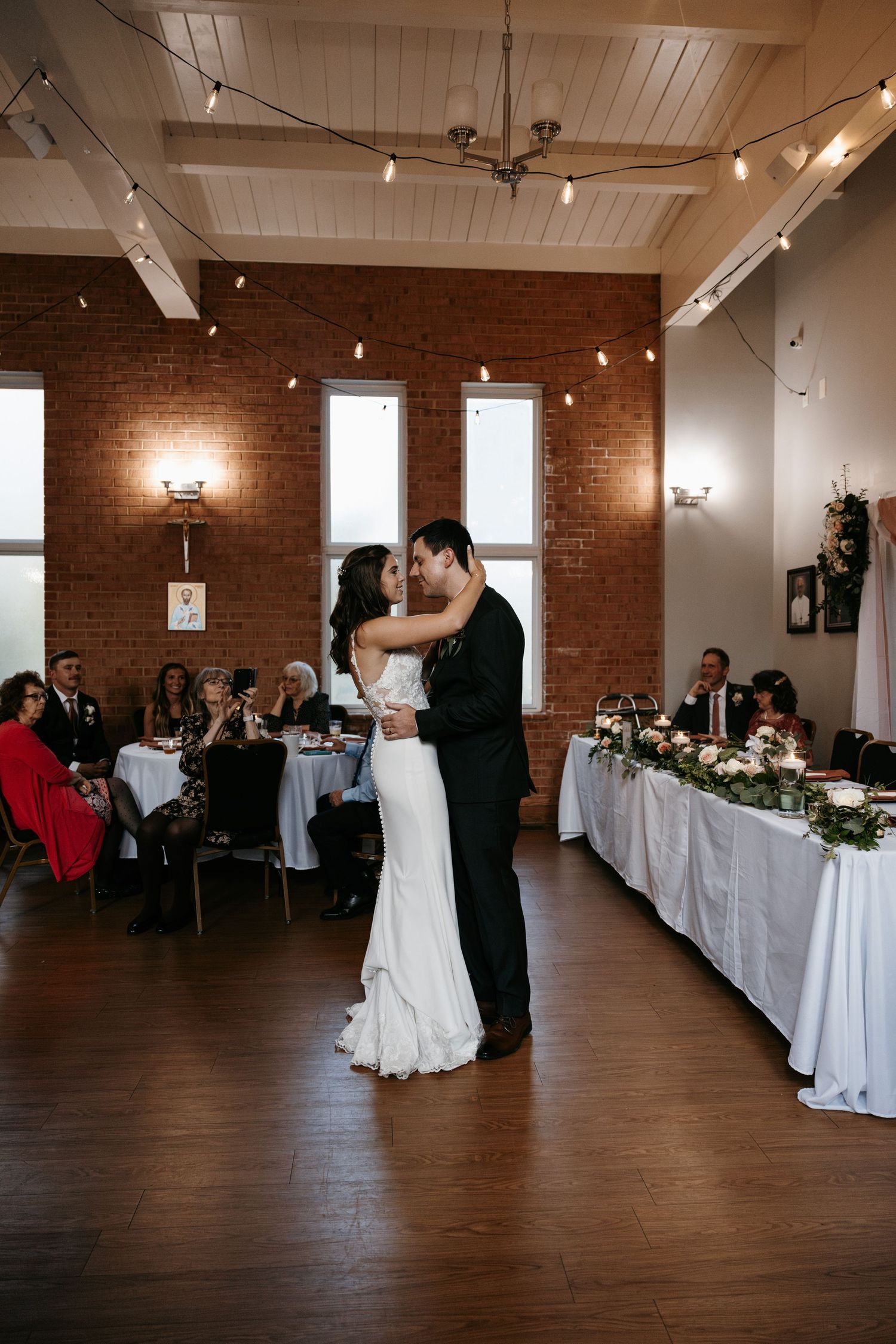Couple shares their first dance in an industrial-style reception venue with brick walls and wood floors.