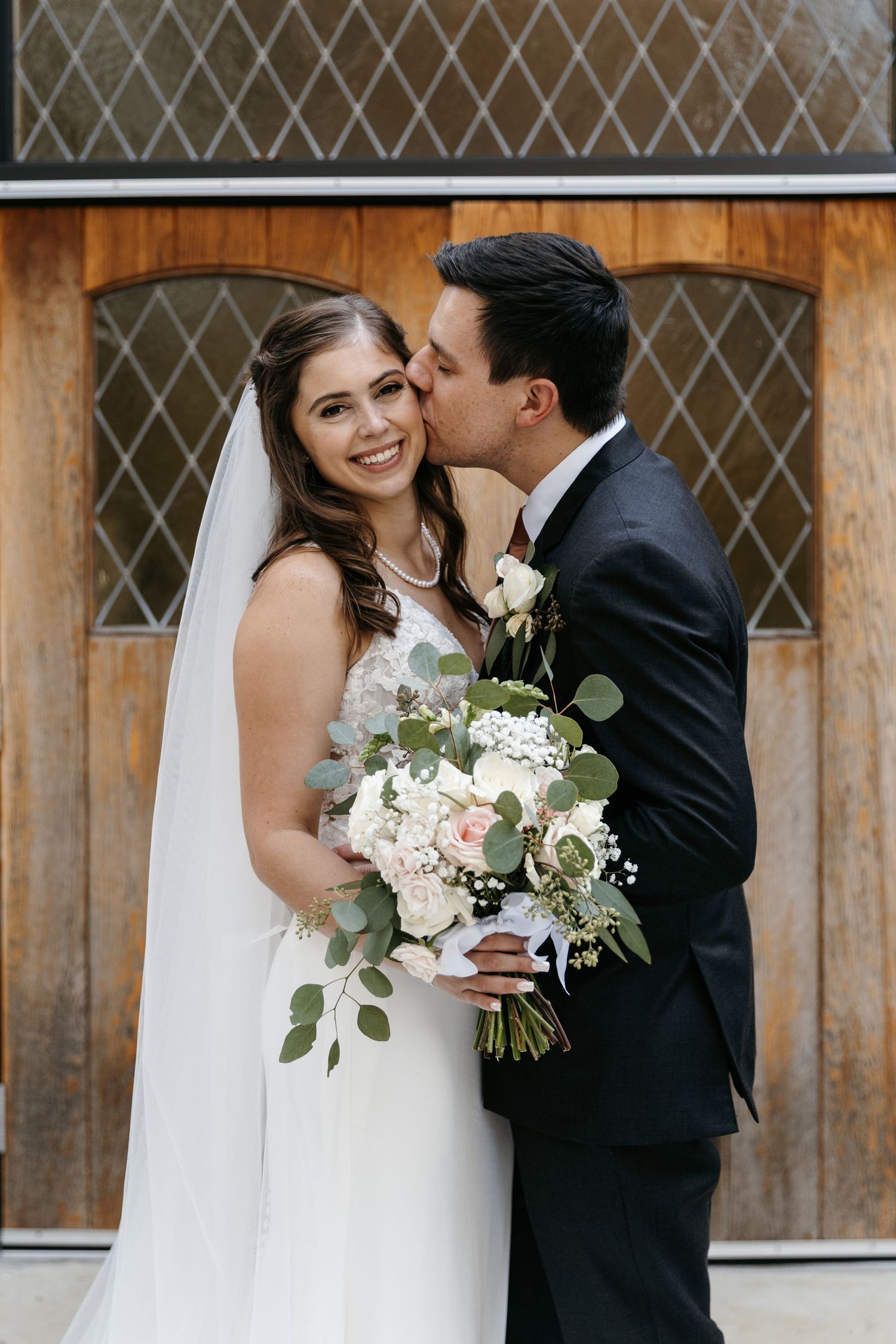 Wedding portrait featuring elegant bouquet with white flowers and eucalyptus against wooden backdrop.