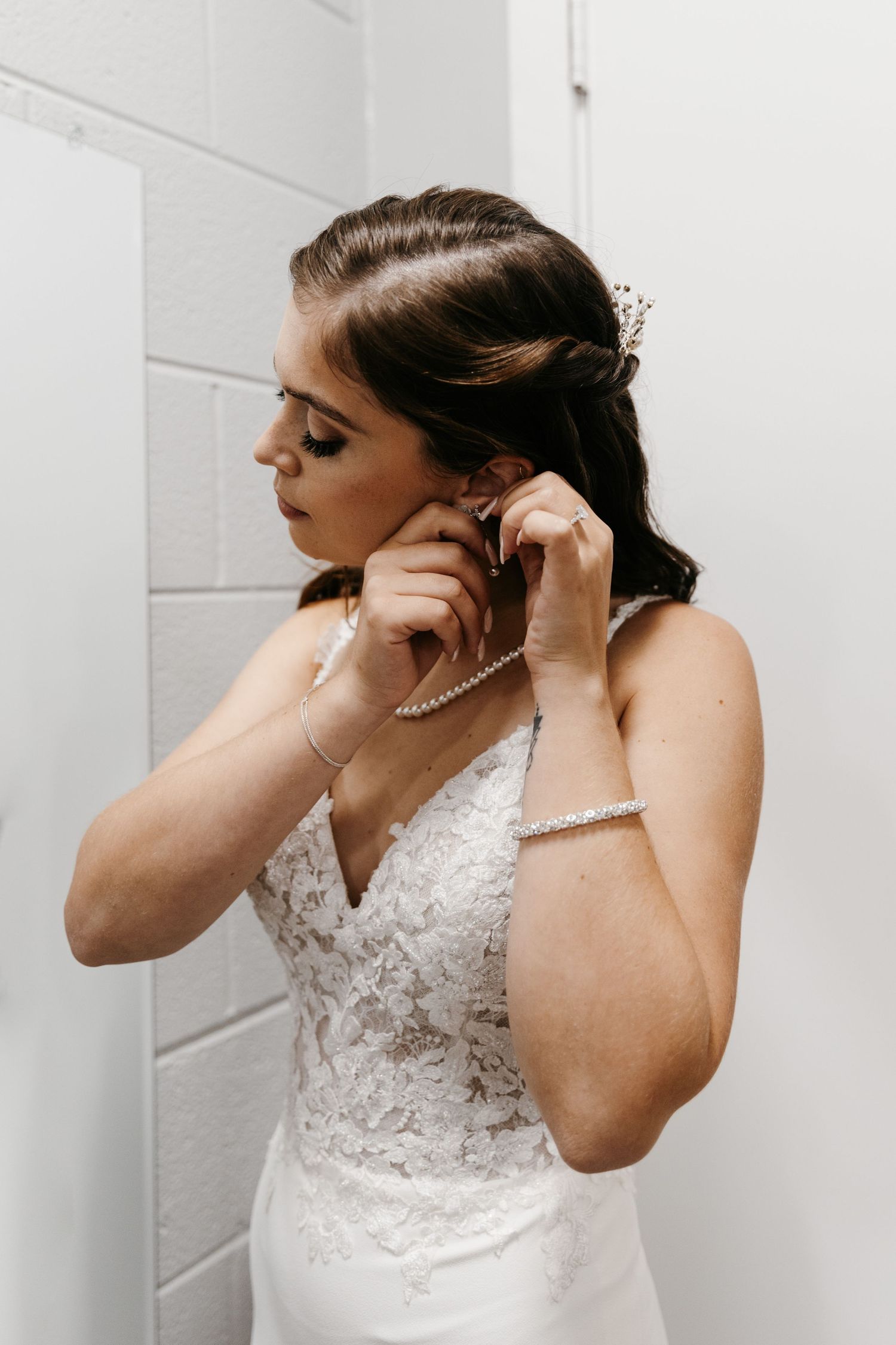 Close up shots of putting on pearl earrings with a lace wedding dress.