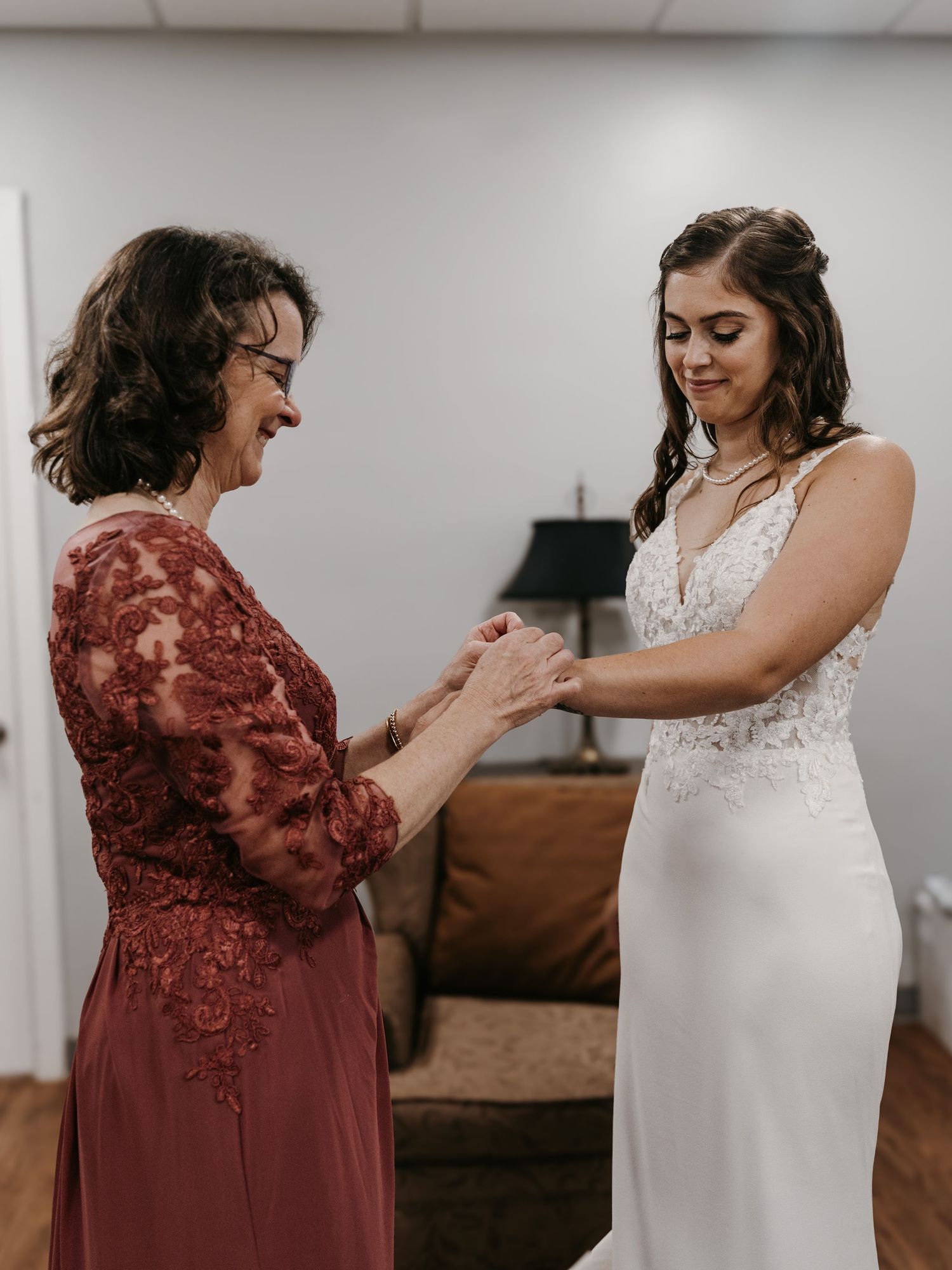 A touching getting ready moment between a bride in white and her mother in burgundy.