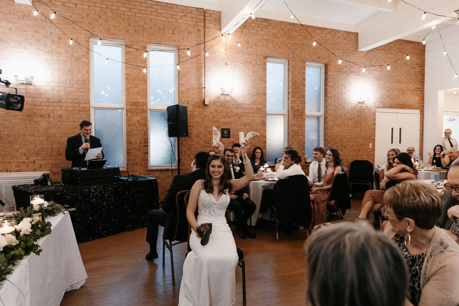 Spacious wedding venue with exposed brick walls, string lights, and guests enjoying the celebration.
