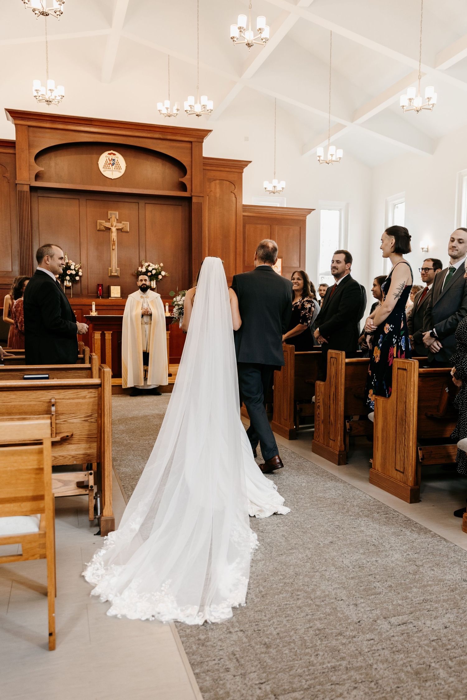 A wedding ceremony in progress inside a traditional church with wooden pews and chandeliers.