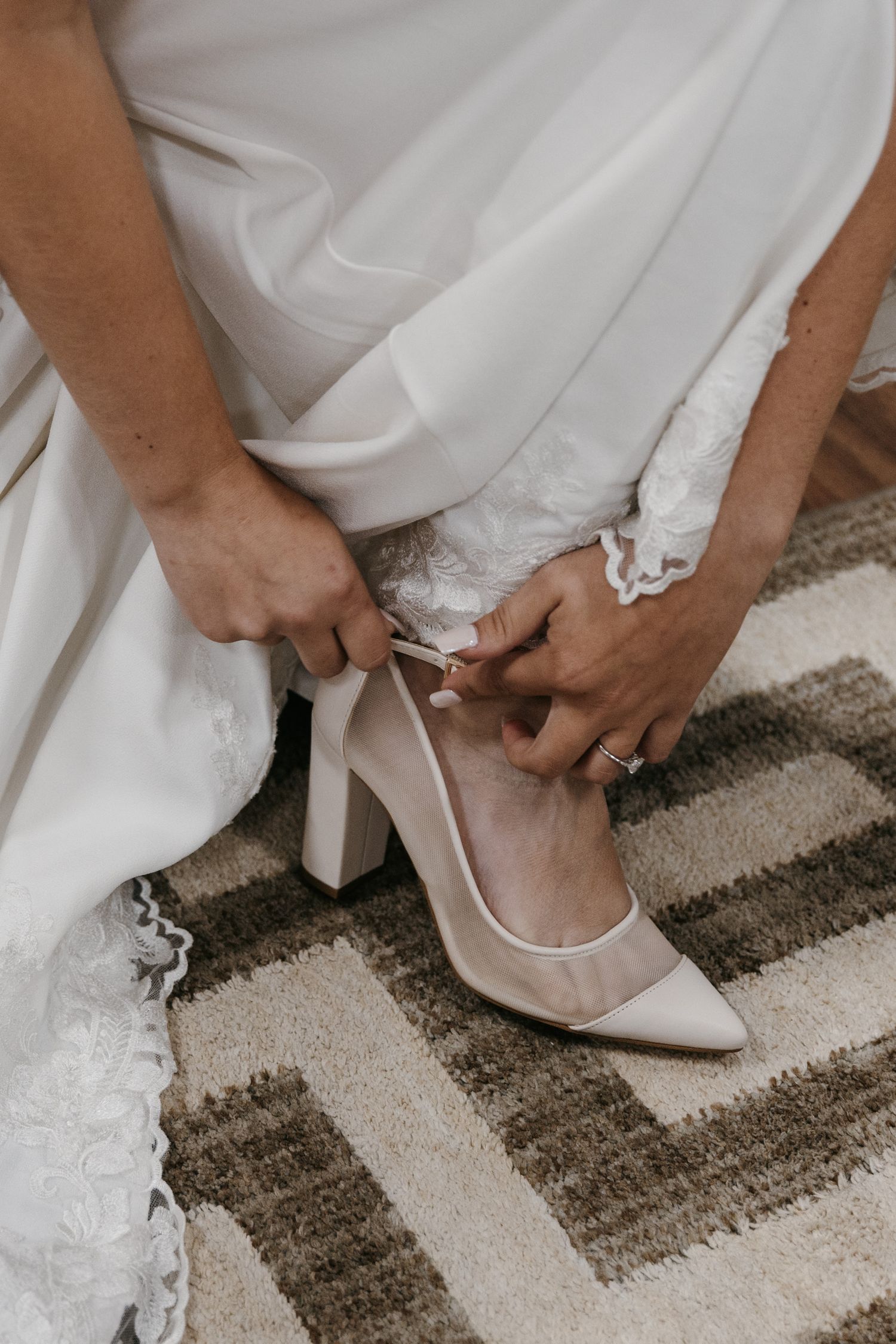 Close-up of white wedding shoes being put on with lace dress details.