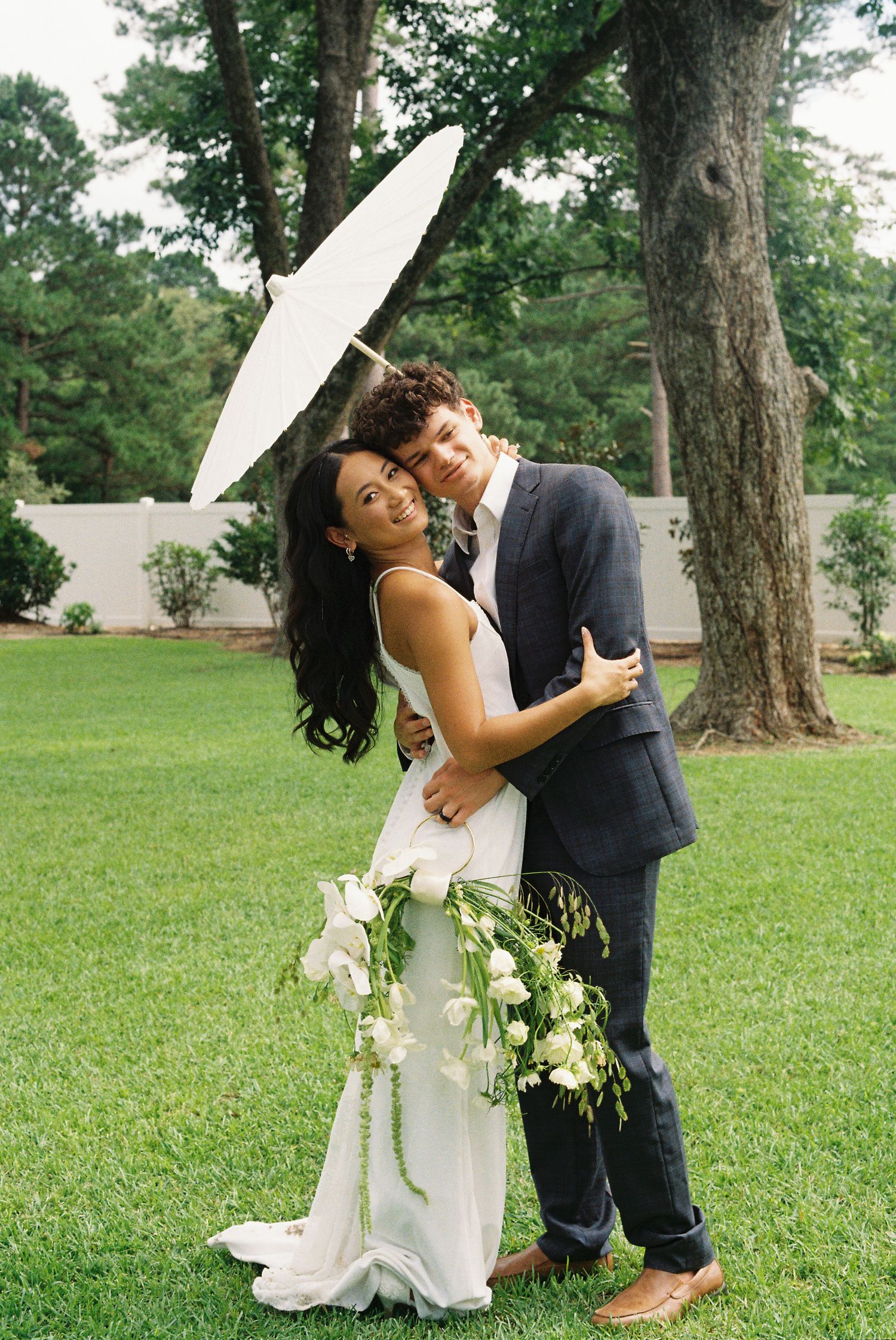 Wedding couple shares intimate dance poses on a grassy lawn with a decorative white parasol.