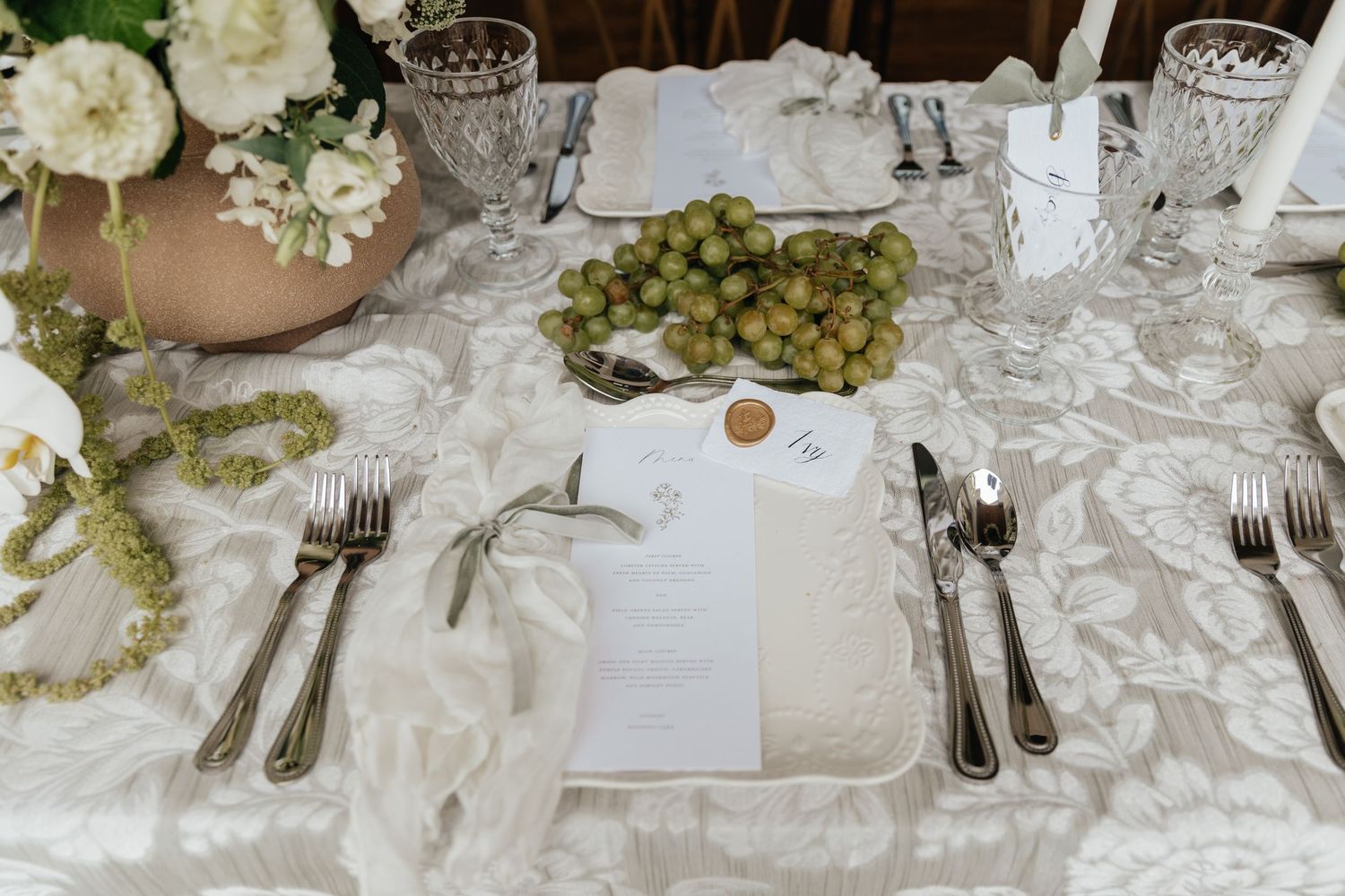 Elegant wedding table setting with white floral arrangements and crystal glassware on a lace tablecloth.