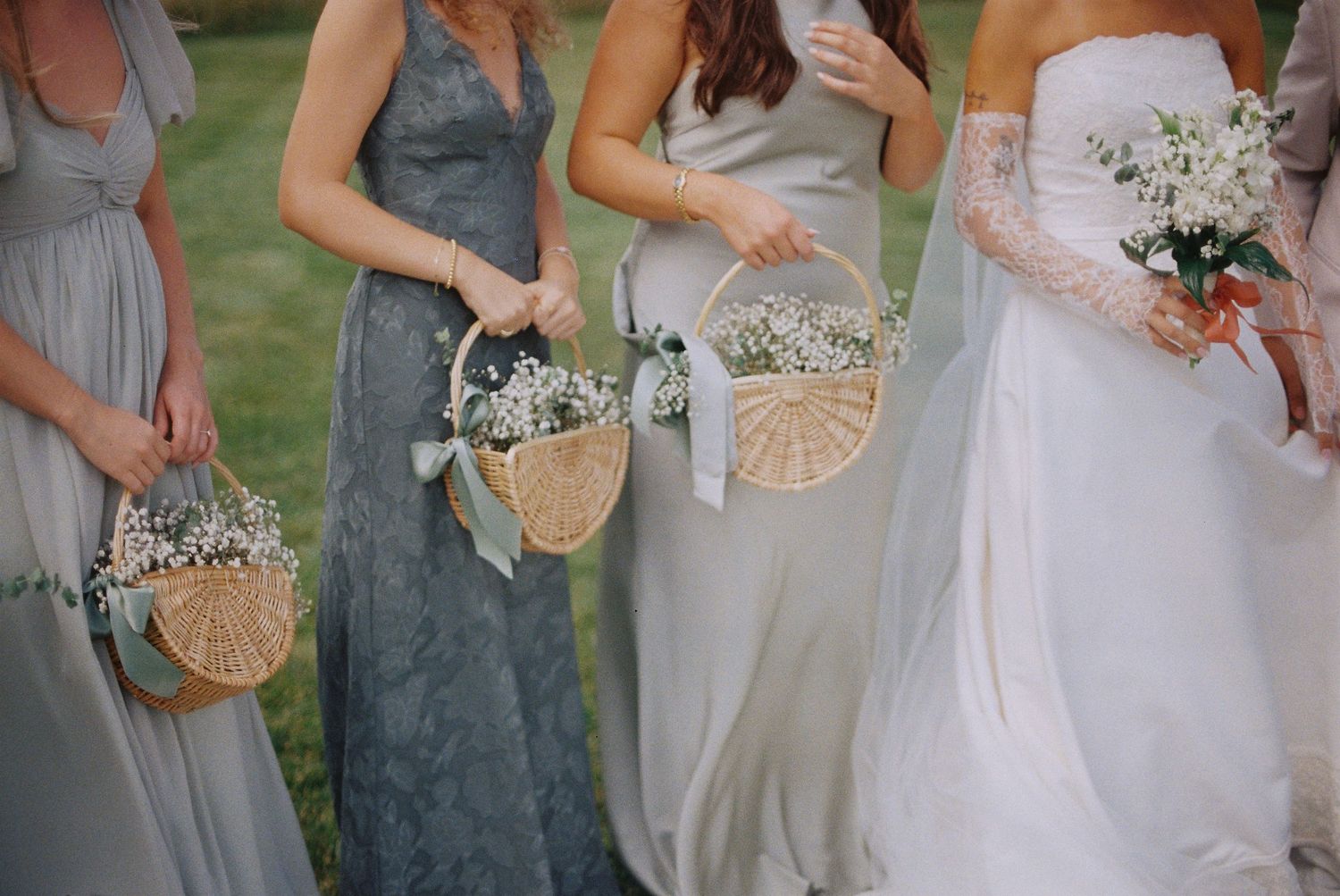 Close up of bride and bridesmaids in sage green dresses holding delicate floral bouquets in baskets.