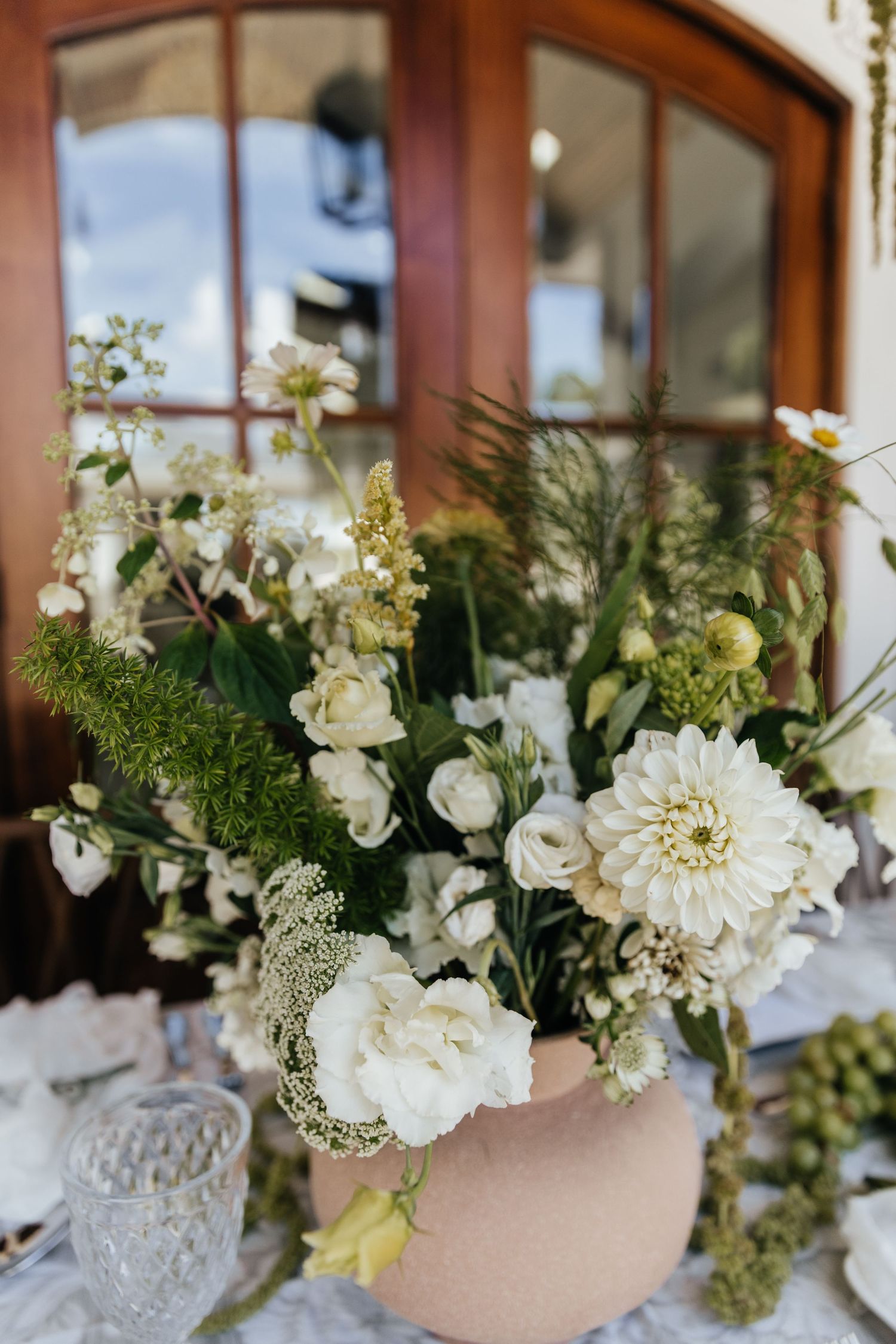 White floral arrangements with delicate blooms and greenery against wooden window frames.