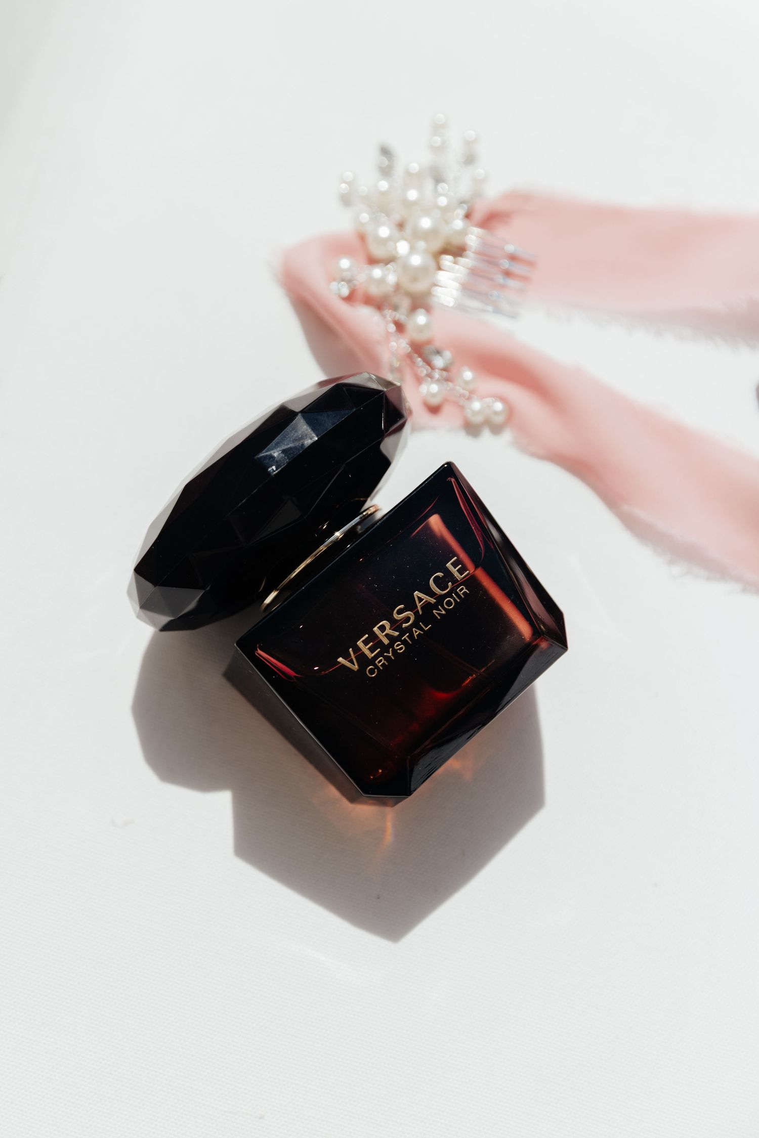 Versace perfume bottle with pearl hair accessory with pink ribbon on white background.