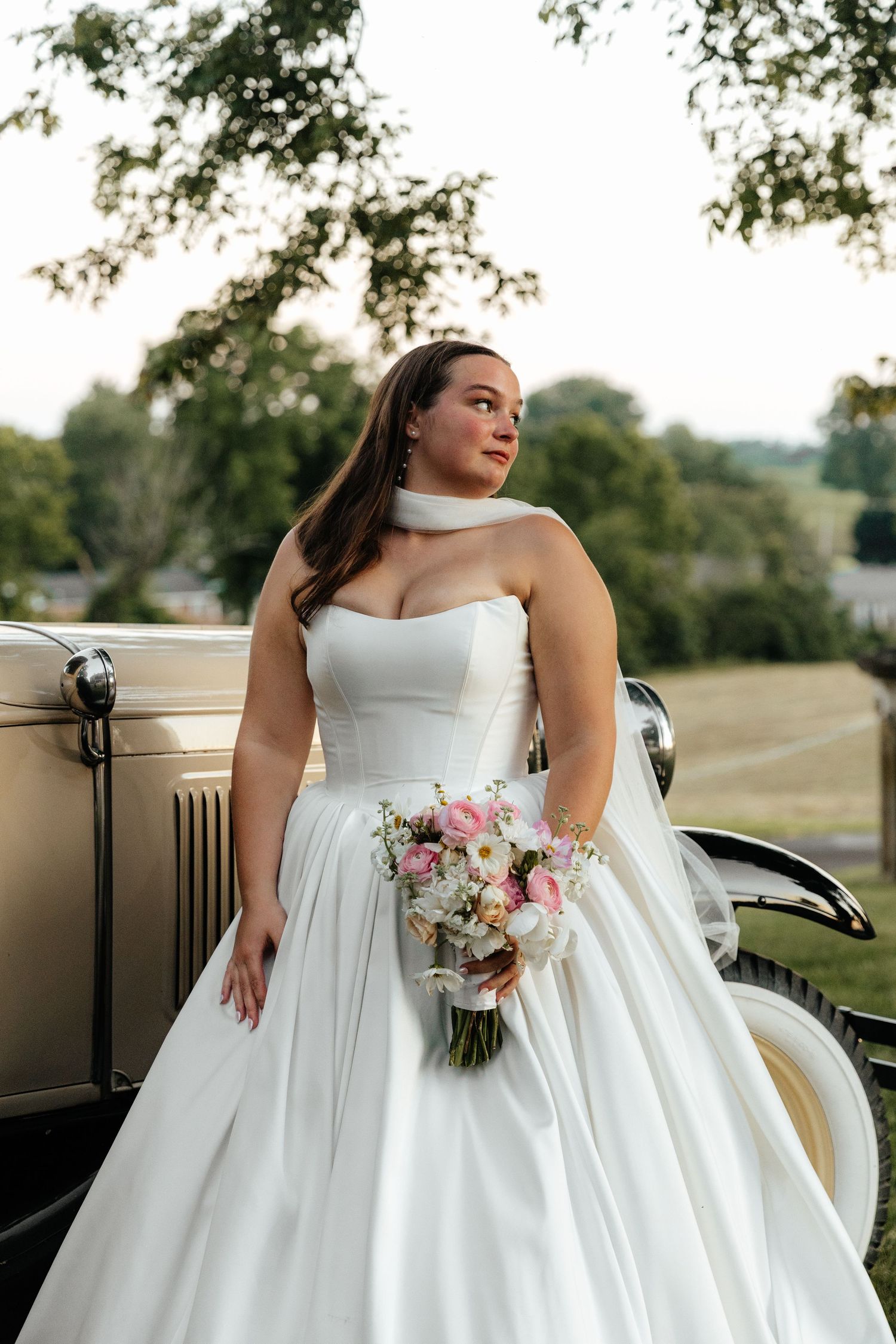 Elegant bridal portrait featuring white ballgown and pink bouquet against outdoor setting.