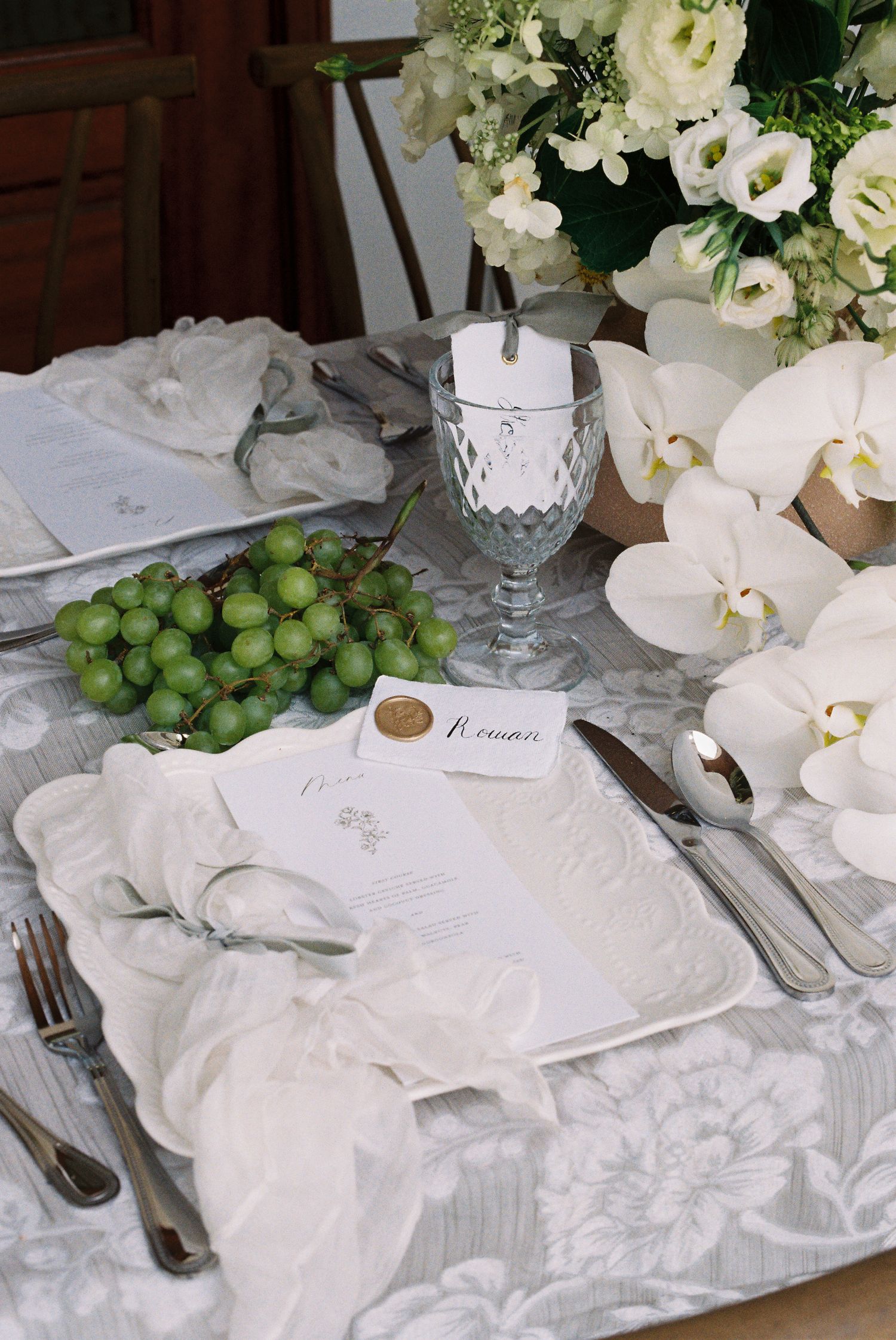 White and green wedding table setting with floral arrangements, crystal glassware, and fine linens.