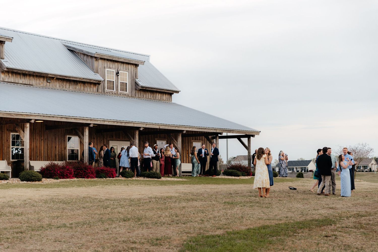 Panoramic view of a rustic barn wedding venue with guests gathered outside.
