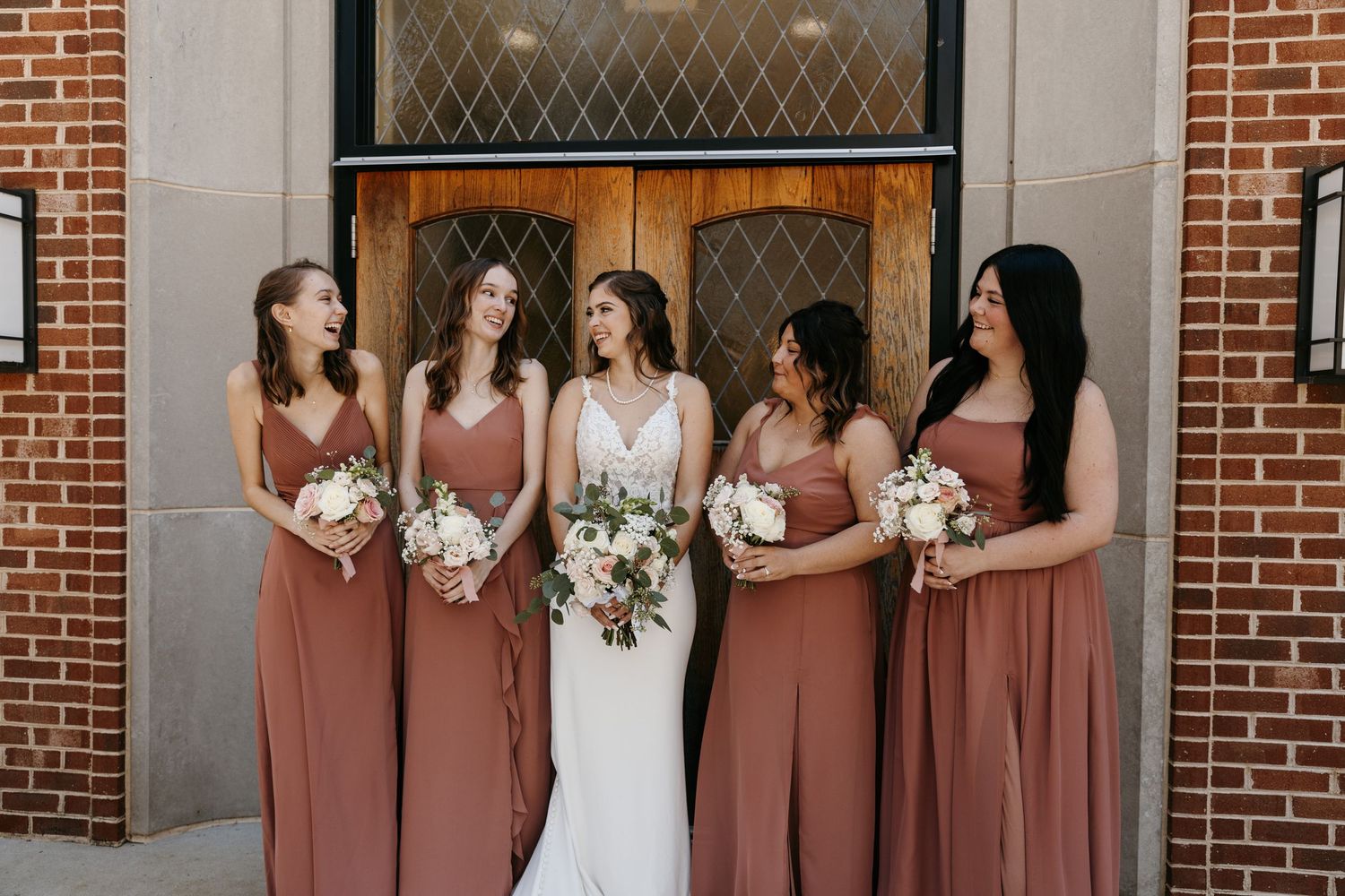 Wedding party poses in front of brick church entrance with classic architectural details.