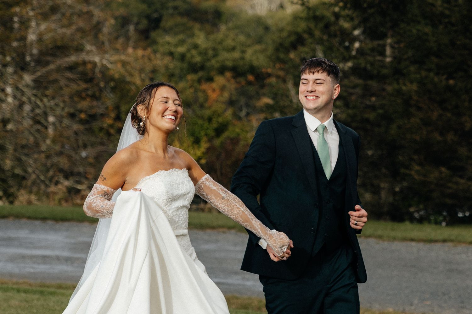 Happy bride and groom holding hands laughing outdoors on their wedding day in elegant attire.