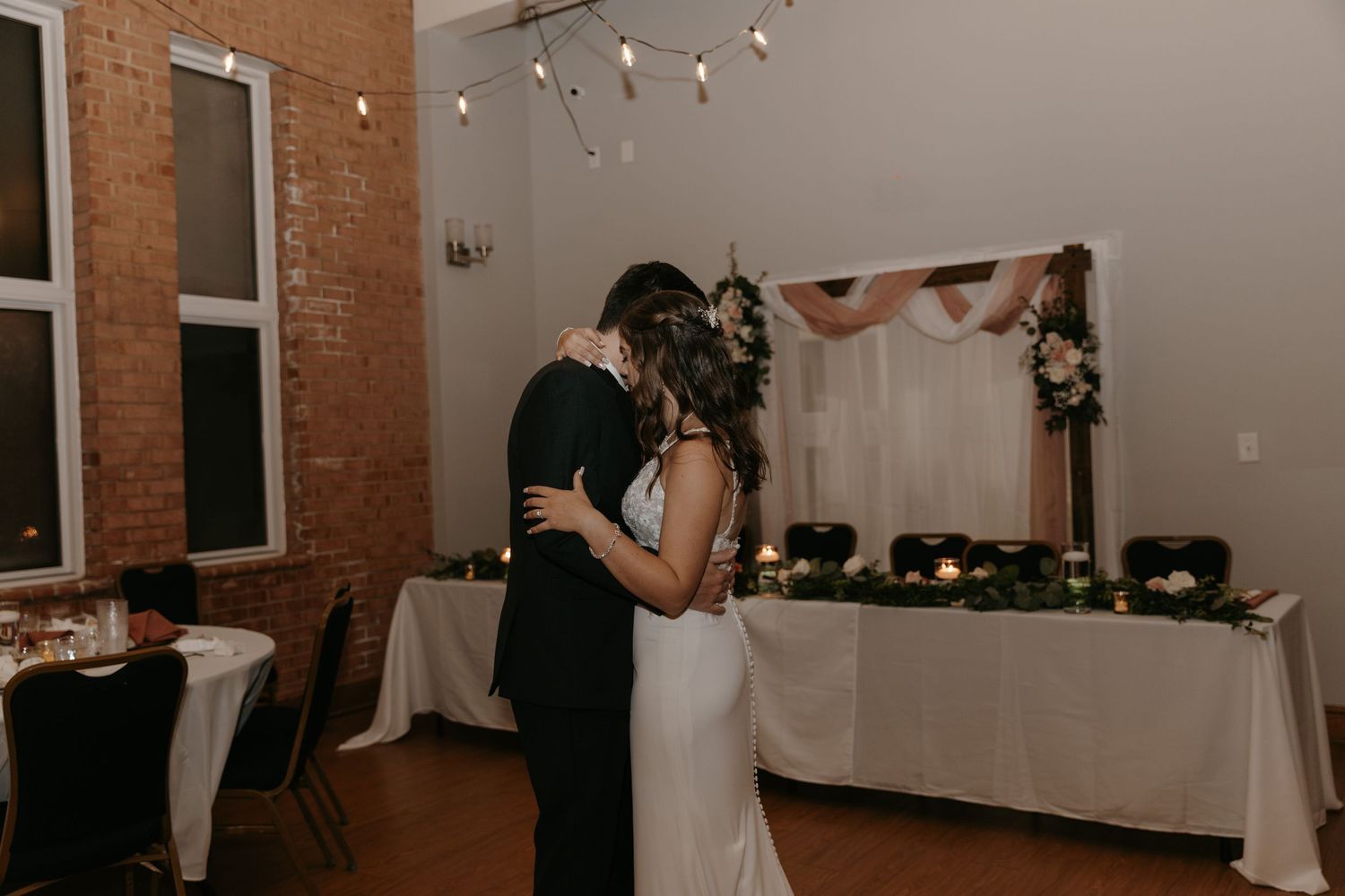A romantic last dance between newlyweds in an industrial-style venue with exposed brick walls.