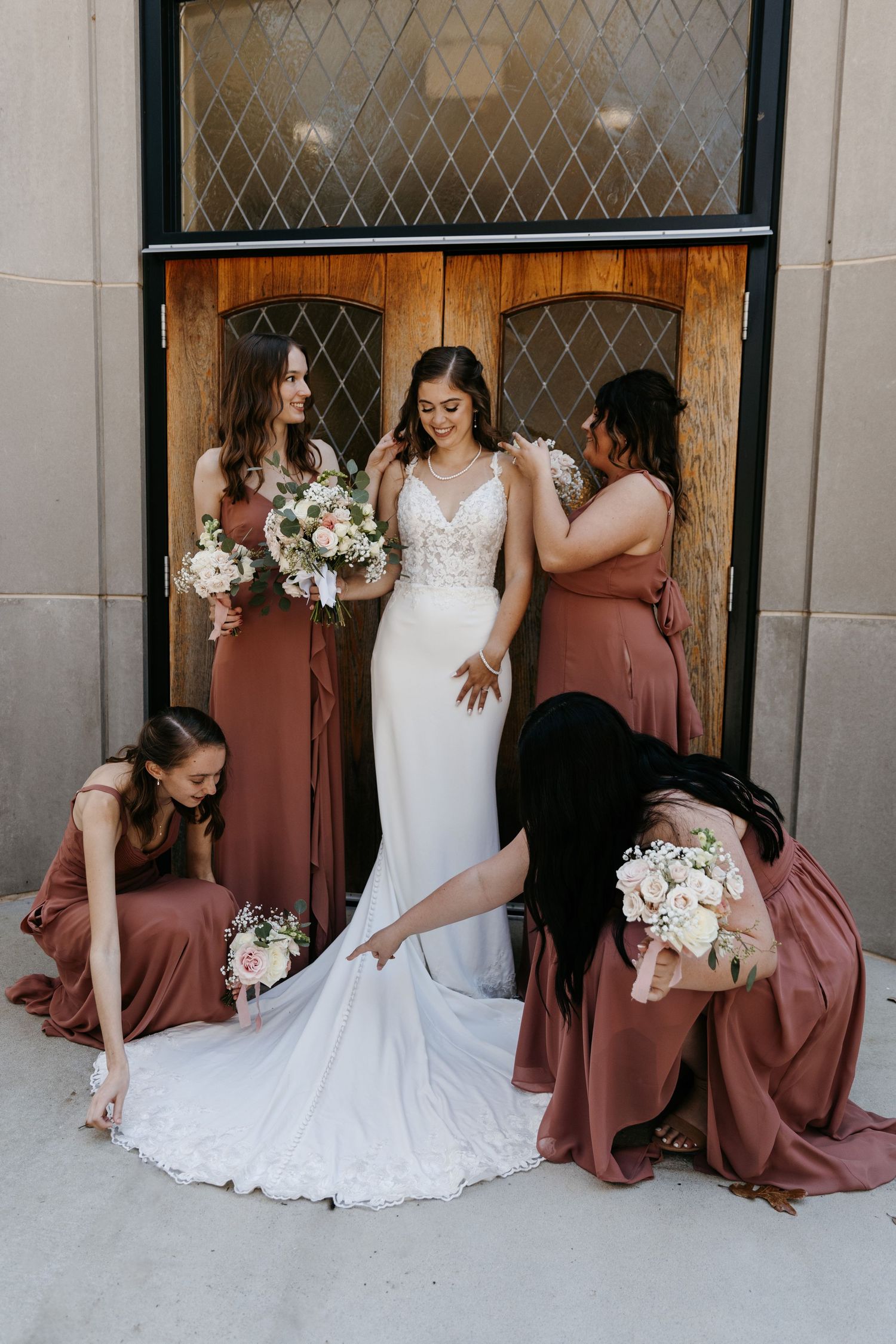 Wedding party creates fun poses for photos against architectural backdrop with white and dusty rose dresses.