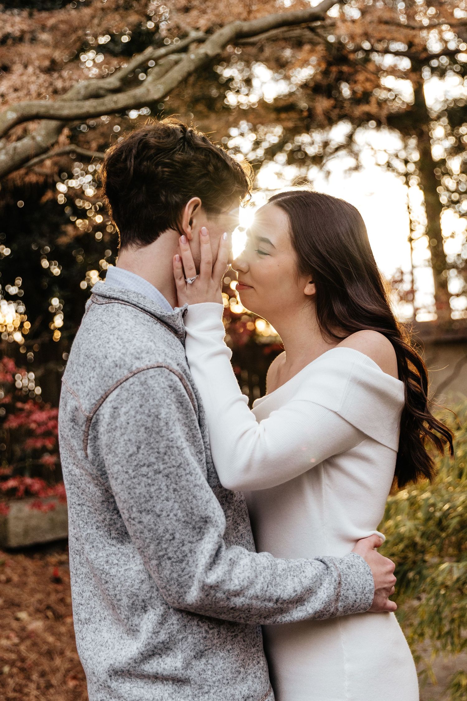 An intimate moment captured between a couple in white and gray clothing during a sunset photoshoot.