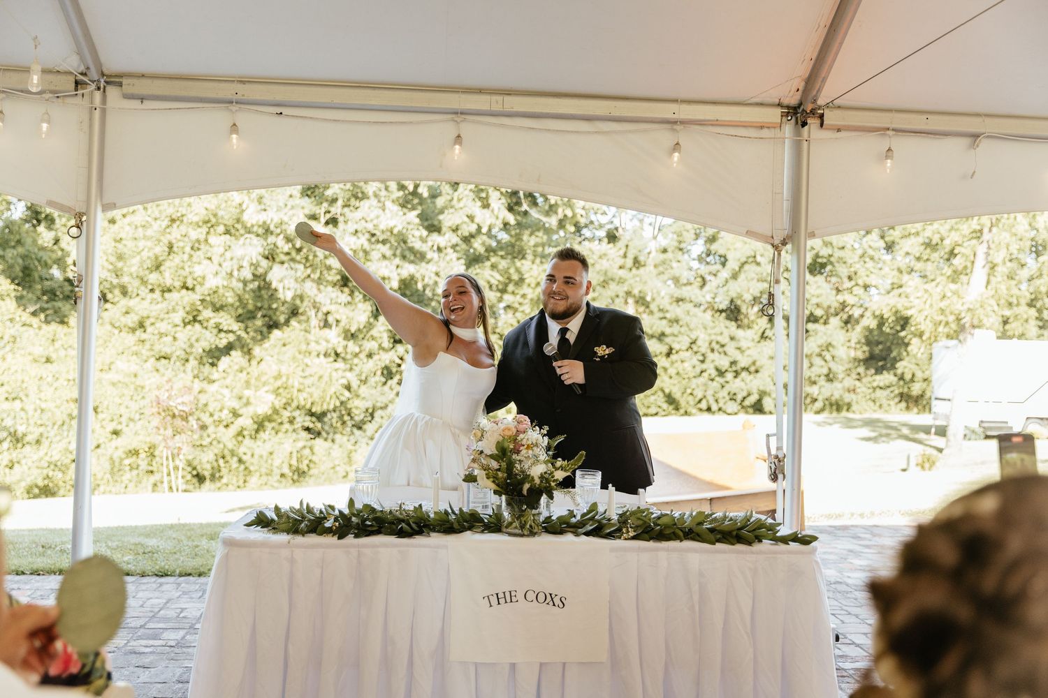 Wedding celebration under white outdoor tent with decorated tables.