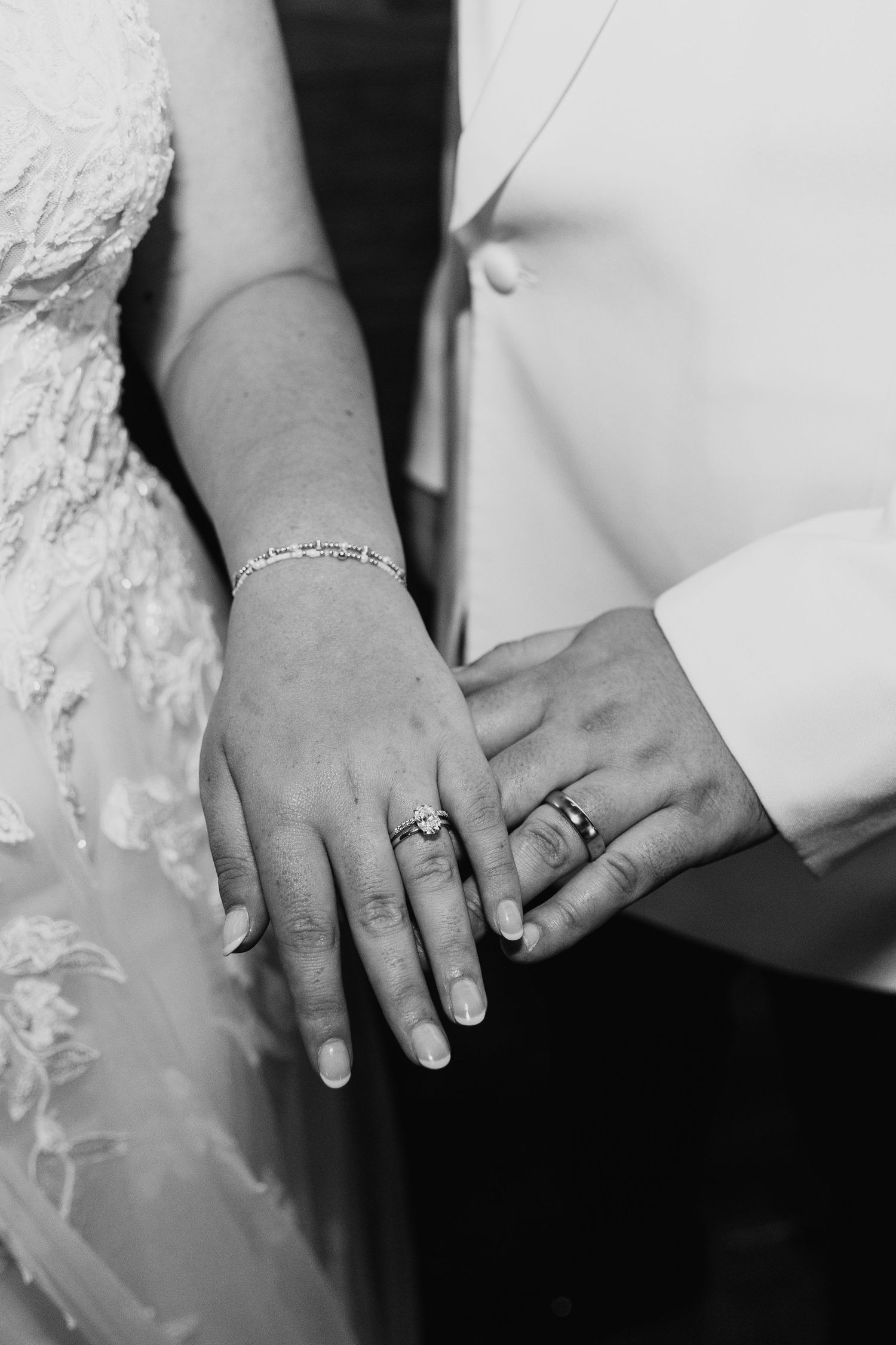 Black and white close-up of wedding rings and hands showing jewelry details.