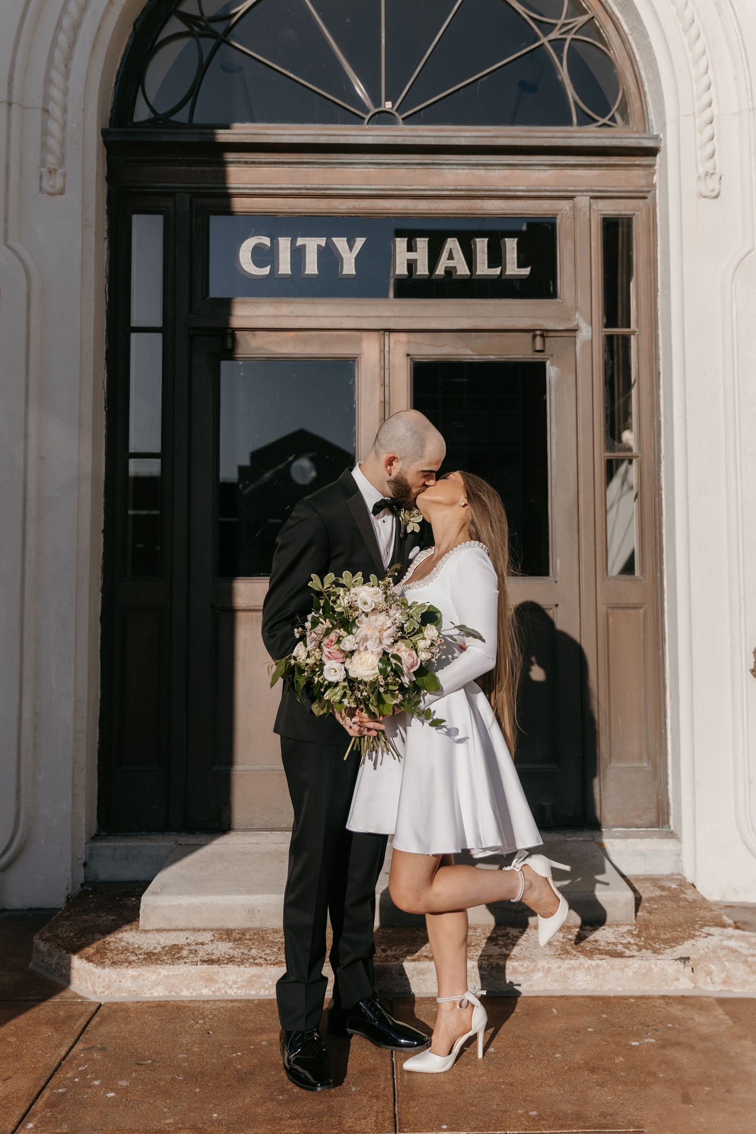 A romantic wedding portrait of a couple sharing an intimate moment at the City Hall entrance.