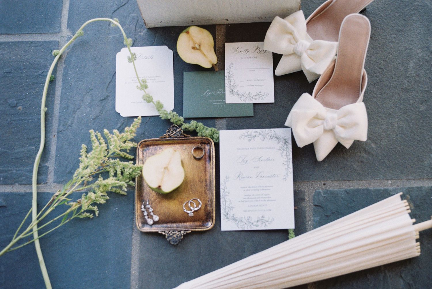 Wedding accessories including shoes and invitations displayed on a stone floor.