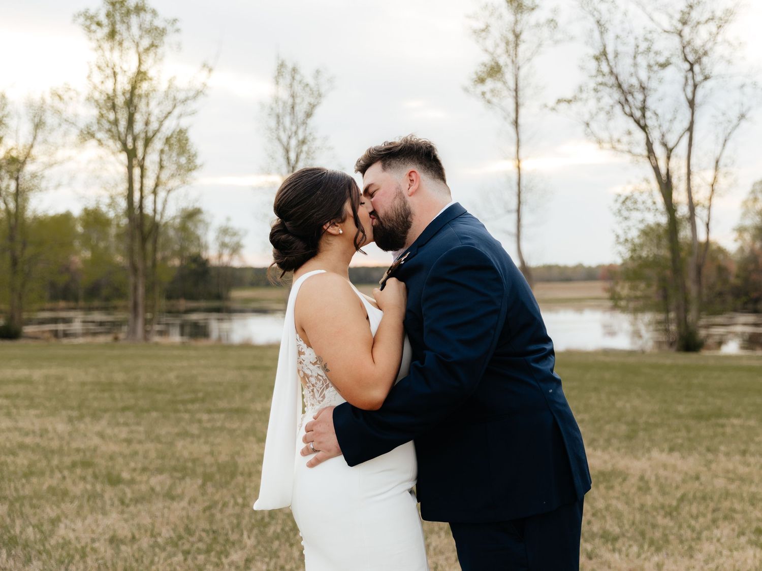 Romantic wedding portrait in an open field with trees and lake in background.