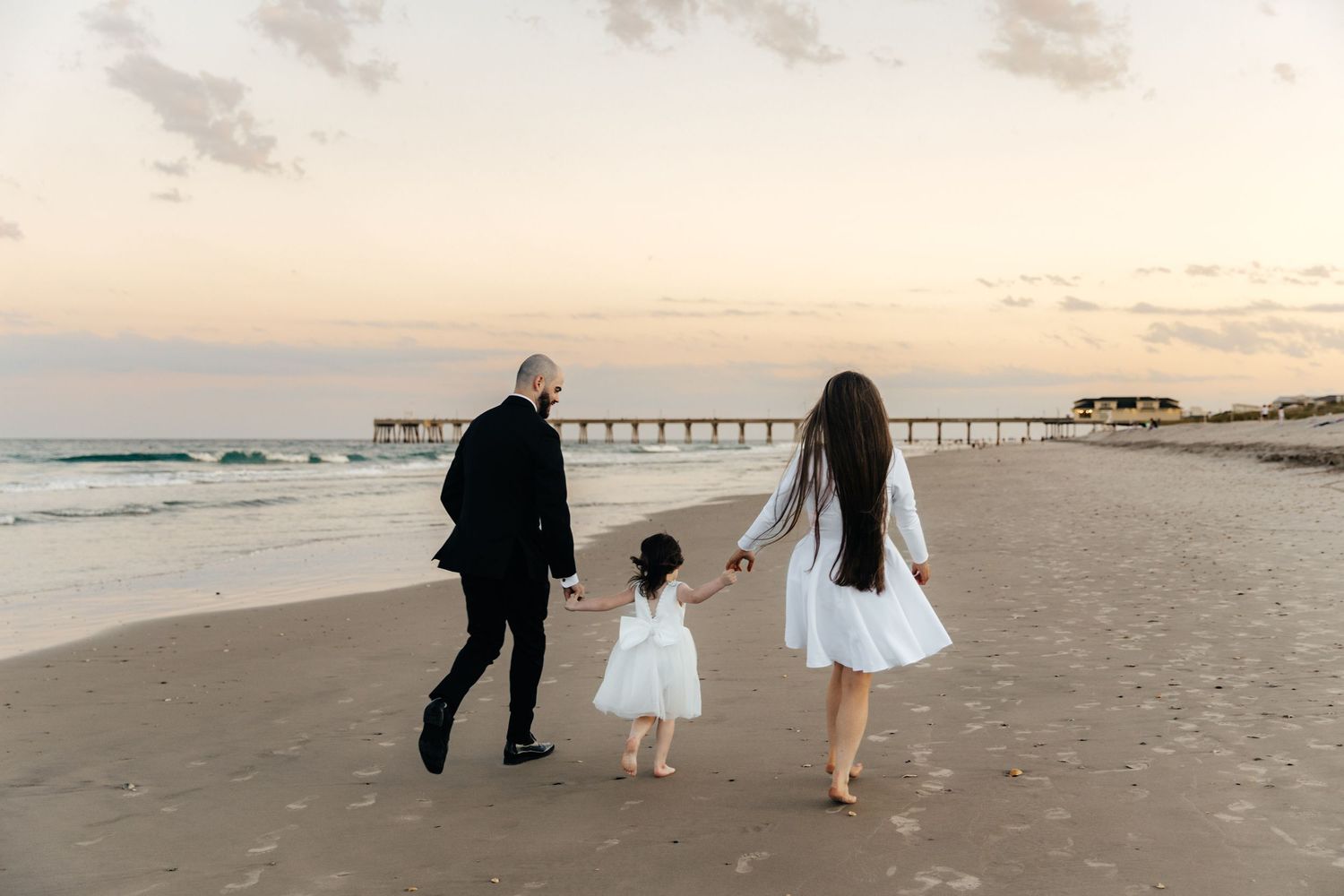 A family walking together on a sandy beach with a pier visible in the distance.