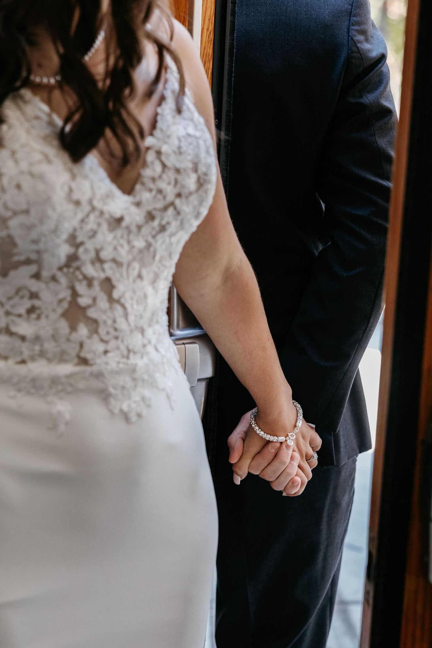 Close-up shot of hands touching through doorway during wedding first look moment.