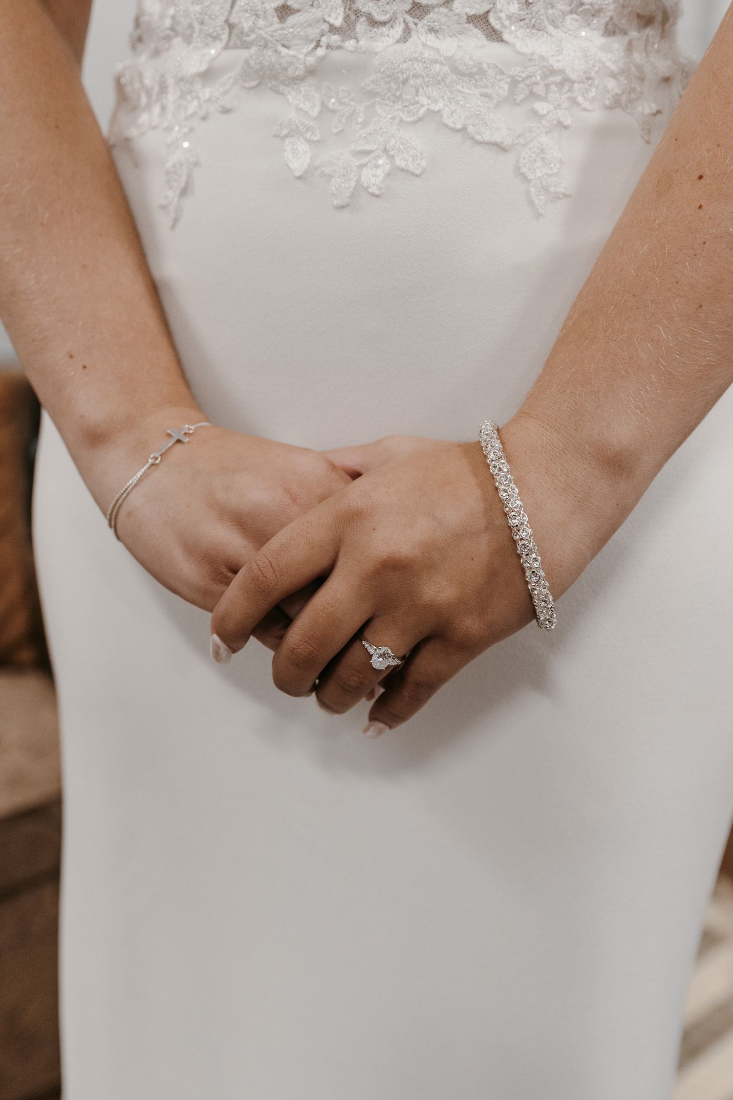 Detail shot of wedding jewelry and rings on hands against a white dress.