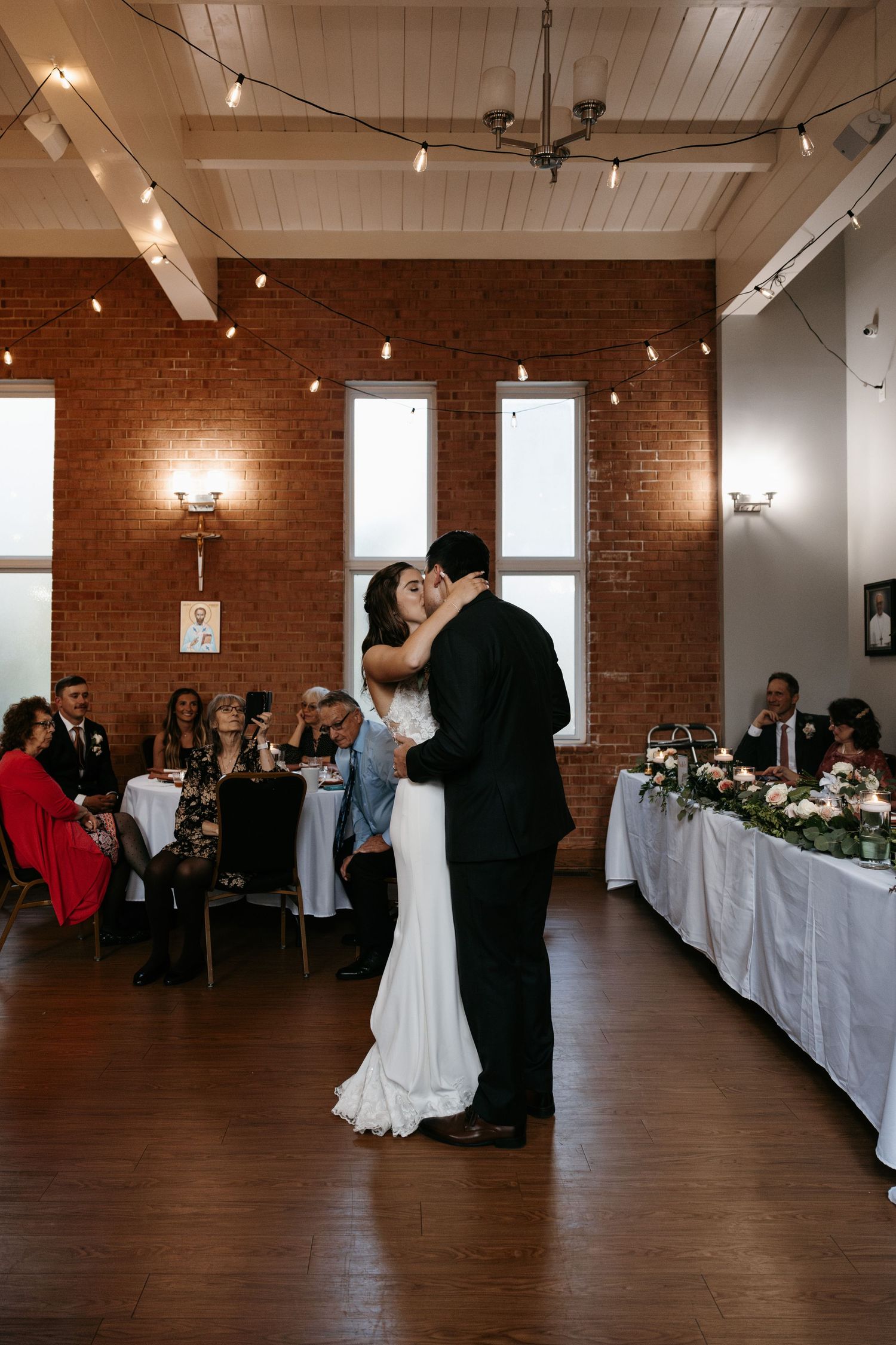 Wedding reception venue with exposed brick walls, string lights, and elegant table settings.