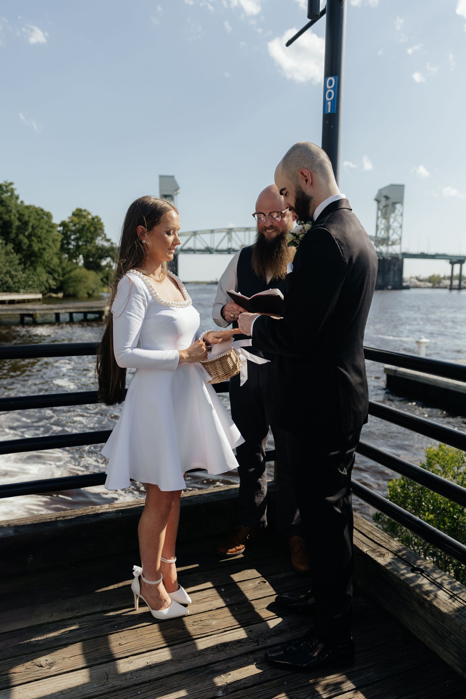 A couple exchanges vows during an intimate waterfront wedding ceremony with a bridge visible in the background.