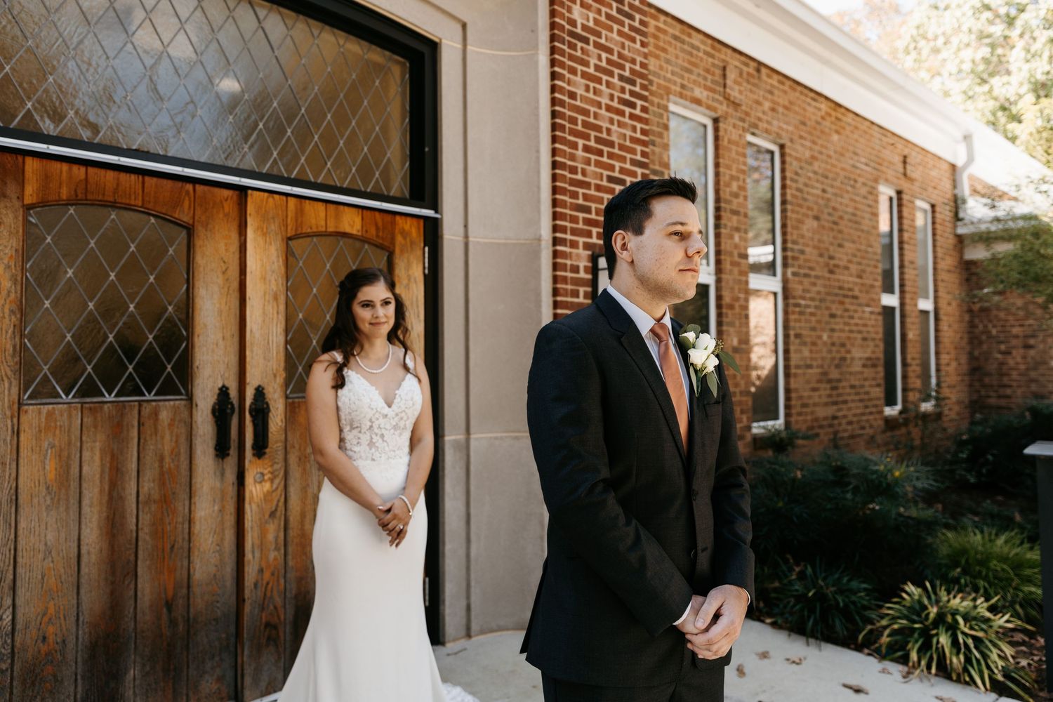 First look wedding photos against brick wall and wooden doors at rustic venue.