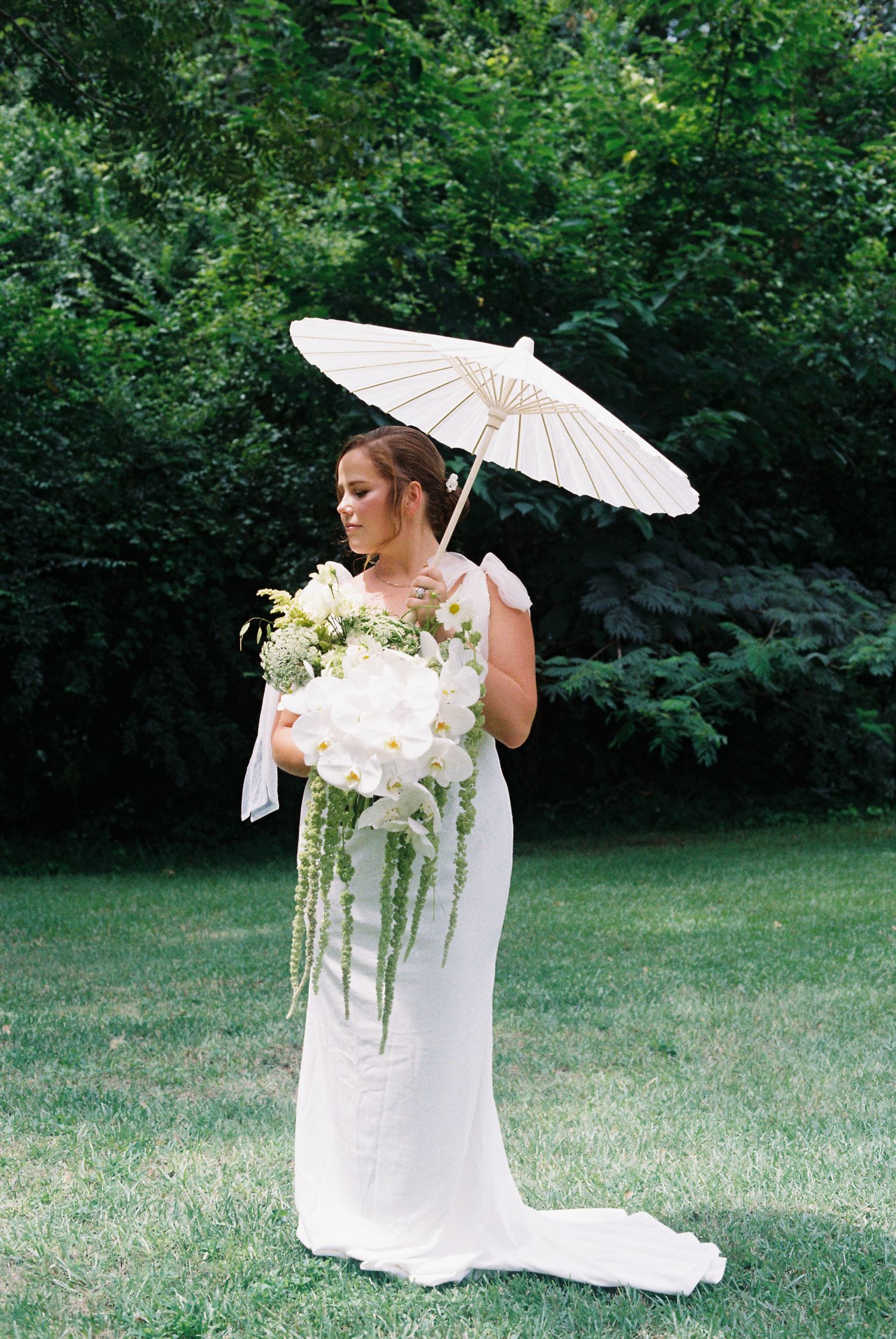 Bride in white dress holding parasol and bouquet during outdoor photo session.