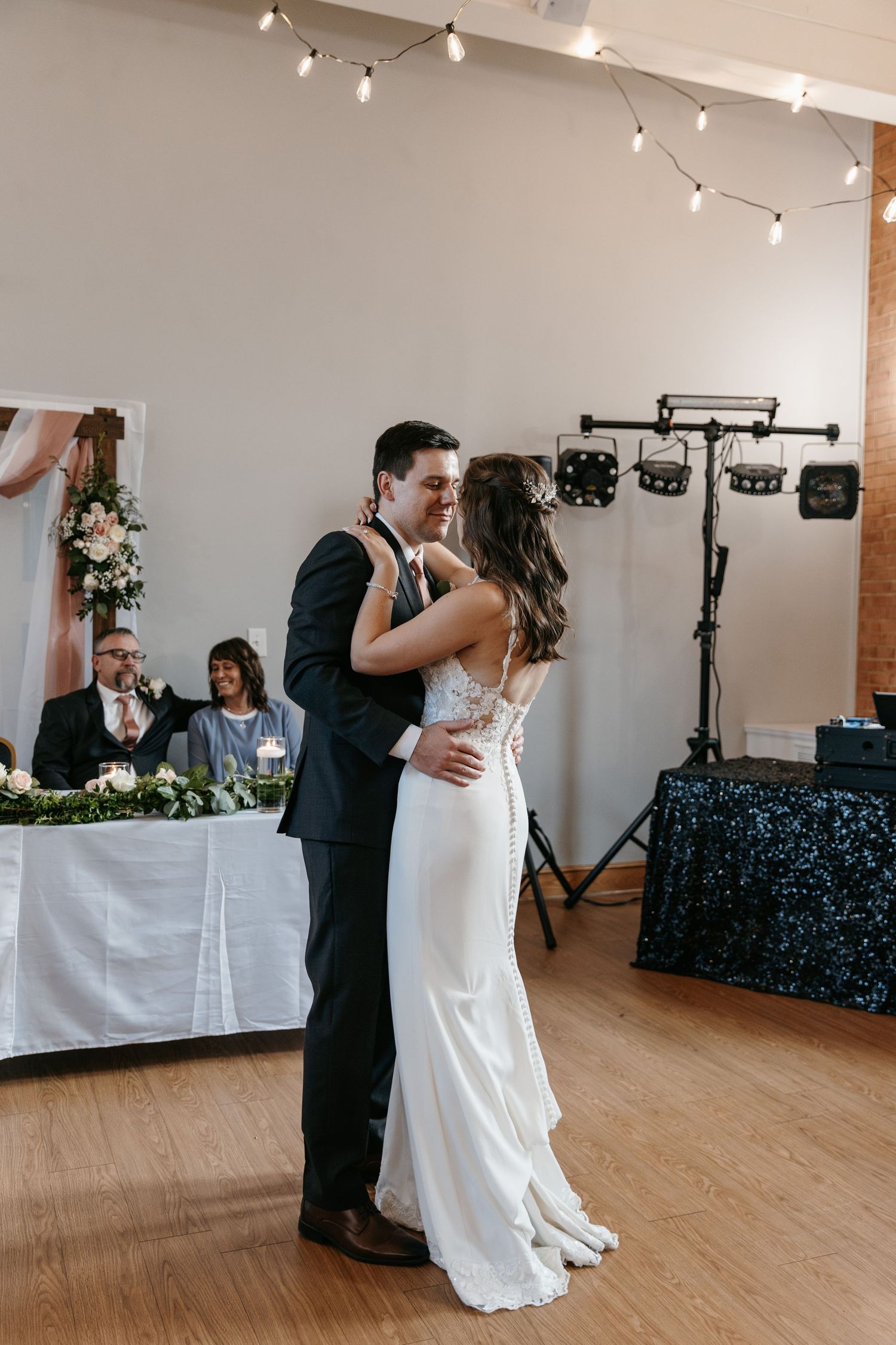 Couple's first dance in reception hall with string lights.