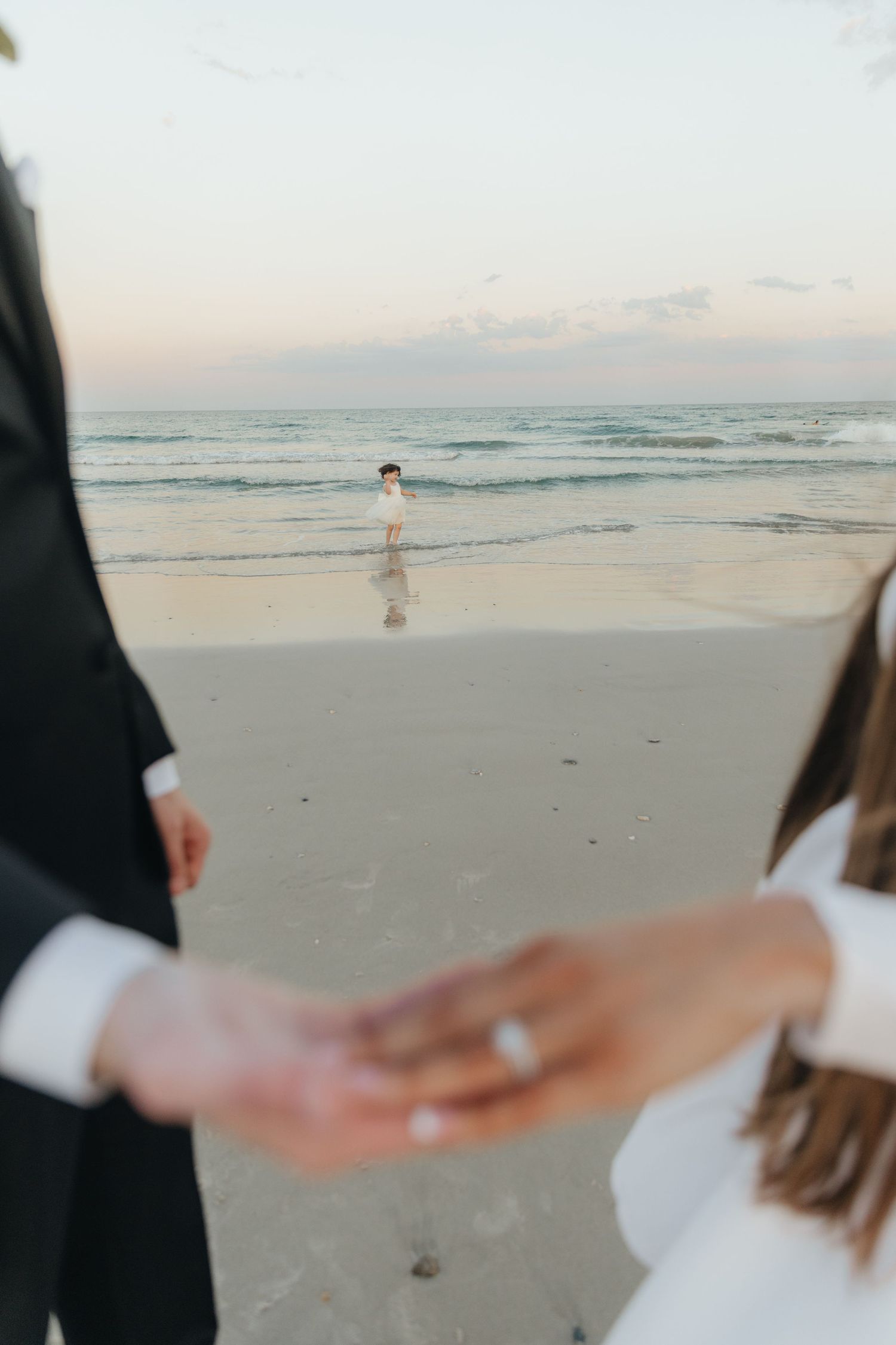 Close-up of newlyweds holding hands on a serene beach at sunset.