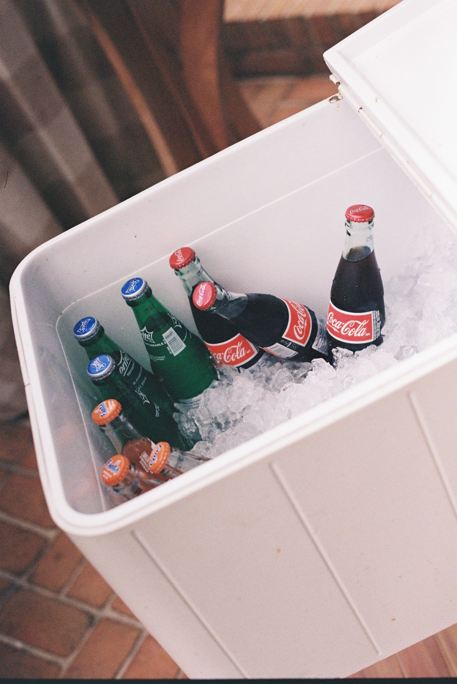 Assorted Coca-Cola and green glass bottles chilling on ice inside a white cooler.